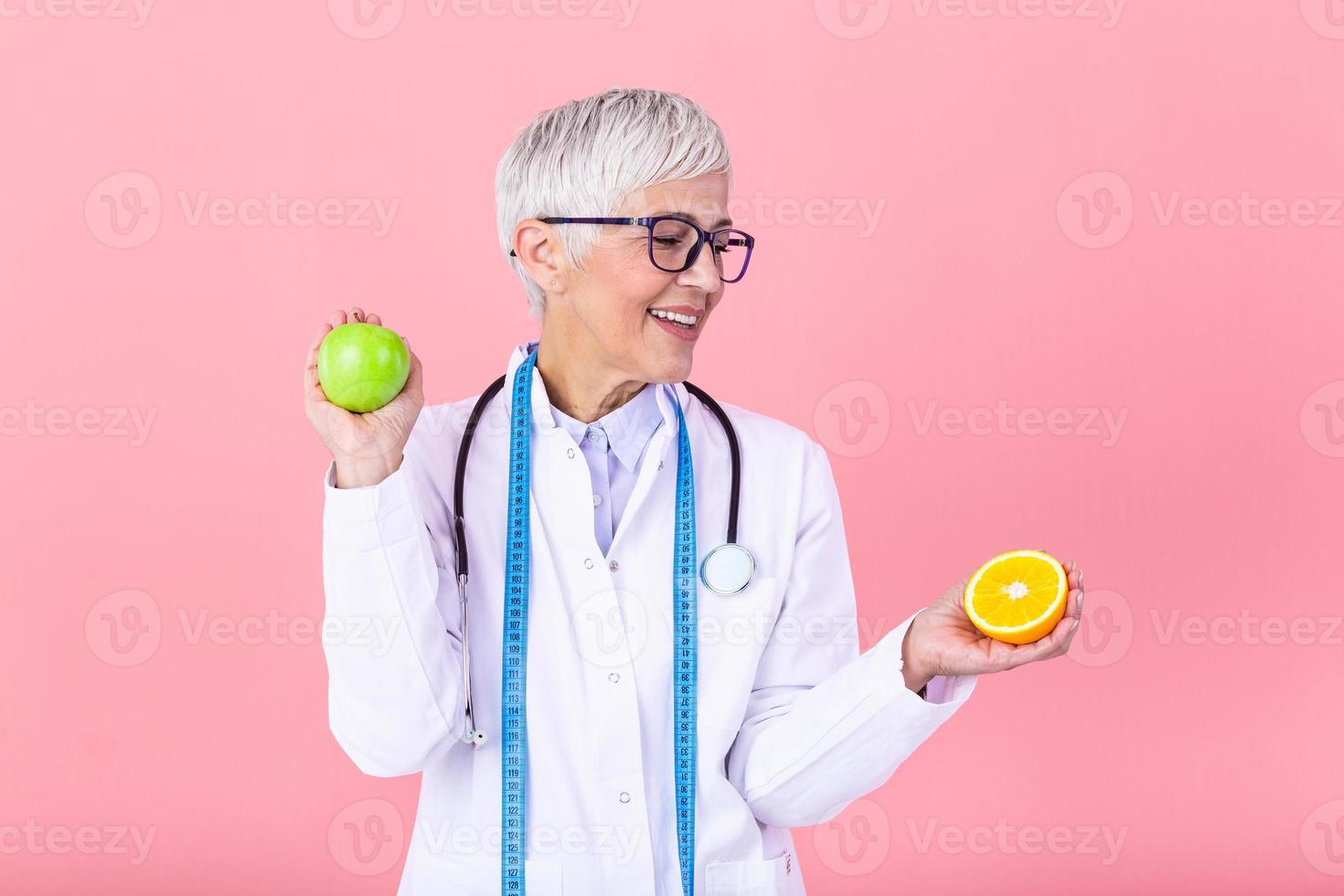Portrait of mature smiling female nutritionist holding an apple isolated. Nutritionist with healthy fruit, juice and measuring tape. Dietitian working on diet plan. photo