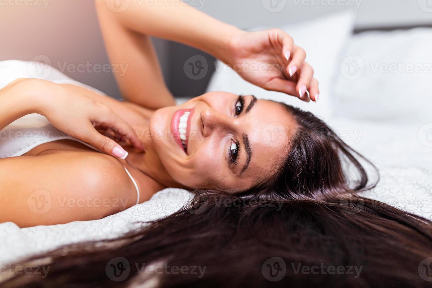 hermosa mujer acostado en cama parte superior vista. contento morena con sano Perfecto pelo sonriente a cámara. belleza, alegría, salud cuidado, Moda concepto foto