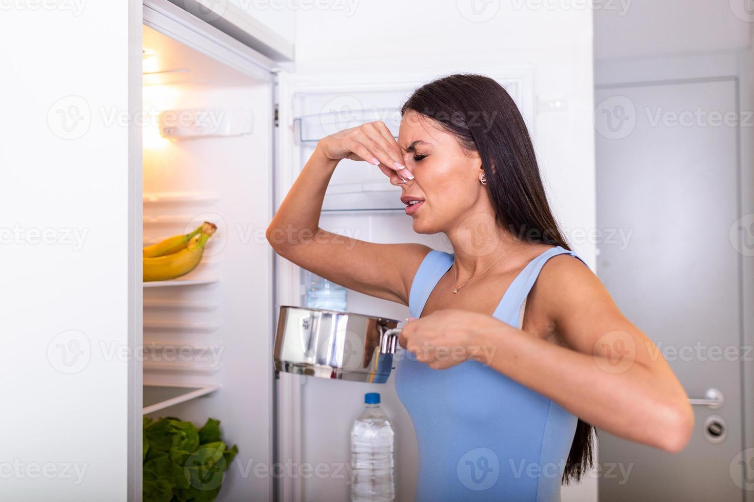 malo comida en refrigerador, joven mujer en participación su nariz porque de malo oler desde comida en refrigerador a hogar foto