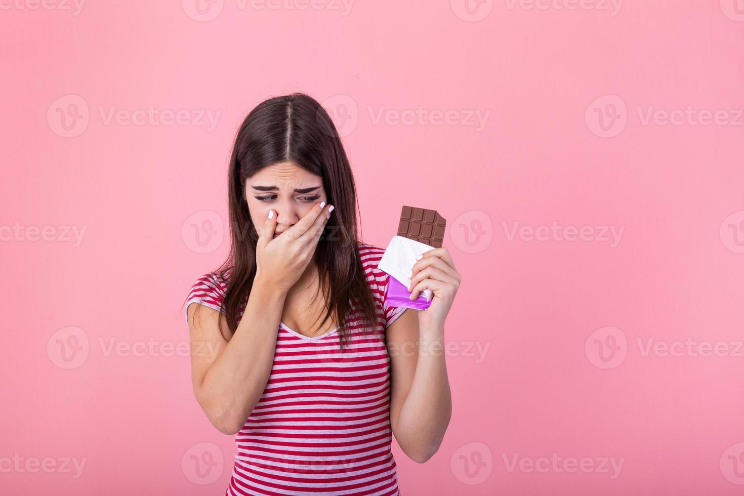 Portrait sad young woman tired of diet restrictions craving sweets chocolate isolated on pink wall background. Human face expression emotion. Nutrition concept. Feeling of guilt. Passion for chocolate photo
