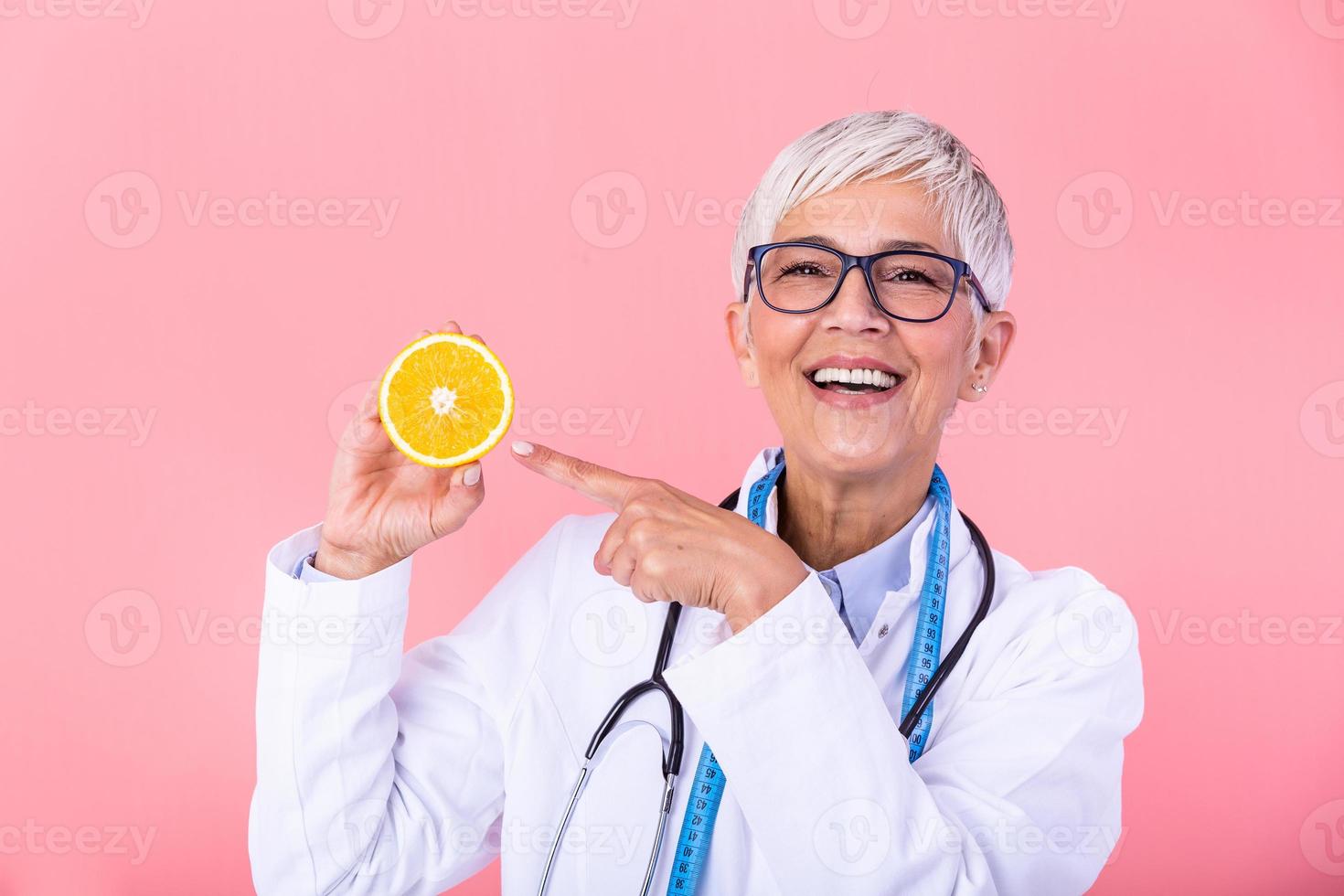 medio Envejecido nutricionista mujer participación naranja Fruta contento con grande sonrisa y dedo señalando a el fruta, nutricionista con sano fruta, jugo y medición cinta. dietético trabajando en dieta plan. foto