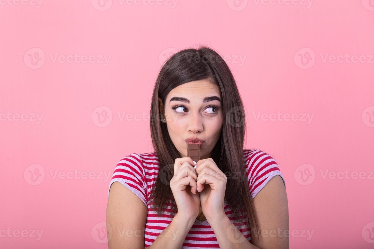 retrato de un contento joven mujer con chocolate bar aislado terminado rosado antecedentes aquelarre su boca. joven mujer con natural hacer arriba teniendo divertido y comiendo chocolate aislado en rosado antecedentes foto