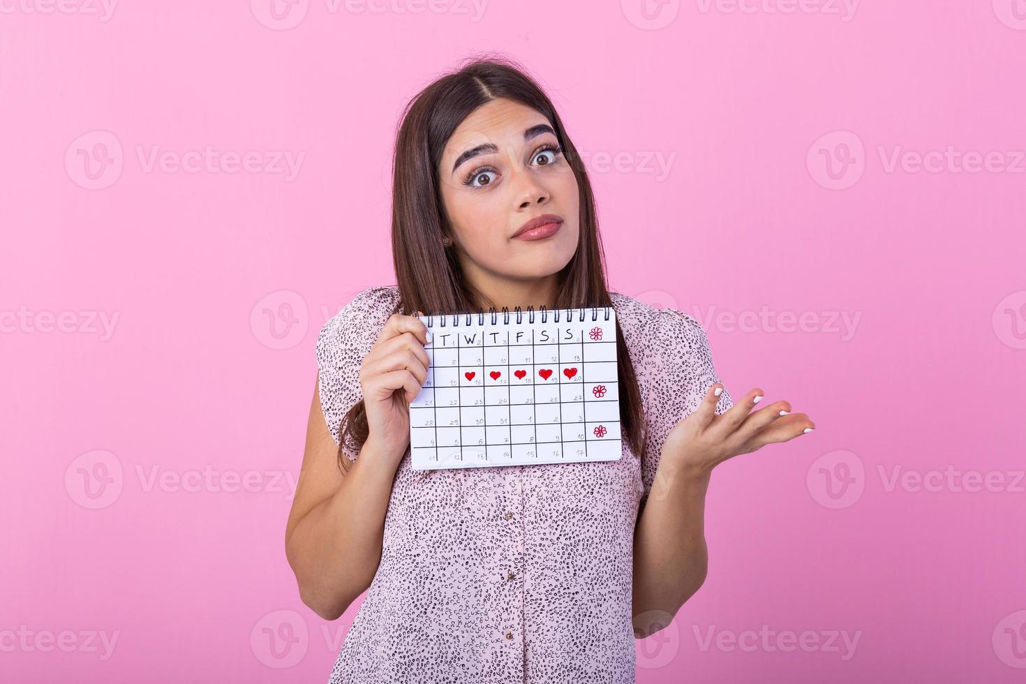 Portrait of young woman in dress, holding female periods calendar for checking menstruation days isolated on trending pink background. Medical healthcare, gynecological concept. photo