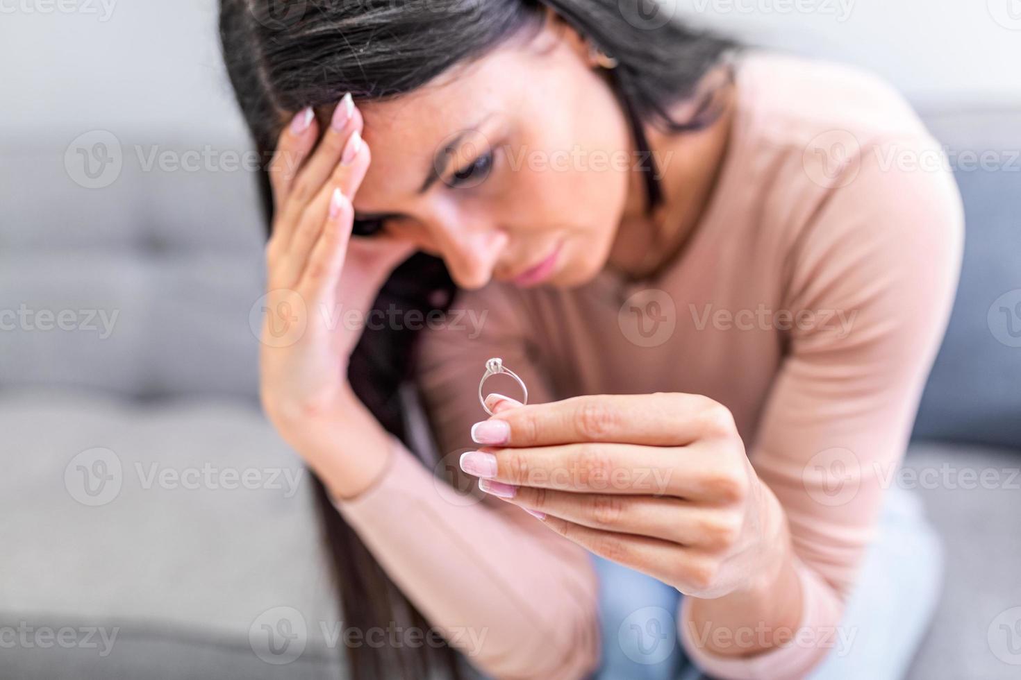 Lonely upset sad thoughtful divorced woman holds gold ring in hands and sits alone at home during problems in life and crisis in relationship. Break up marriage and divorce photo