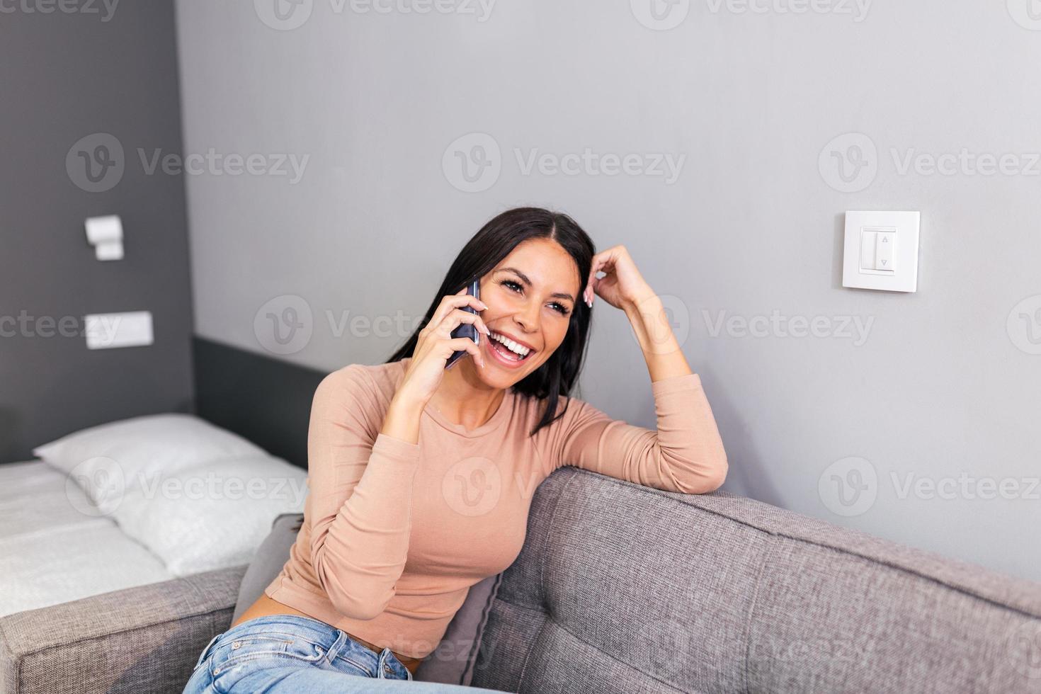 sonriente hermosa mujer hablando en el teléfono a hogar, contento joven niña sostiene Teléfono móvil haciendo respondiendo llamar, atractivo niña teniendo agradable conversacion chateando por móvil con amigo foto