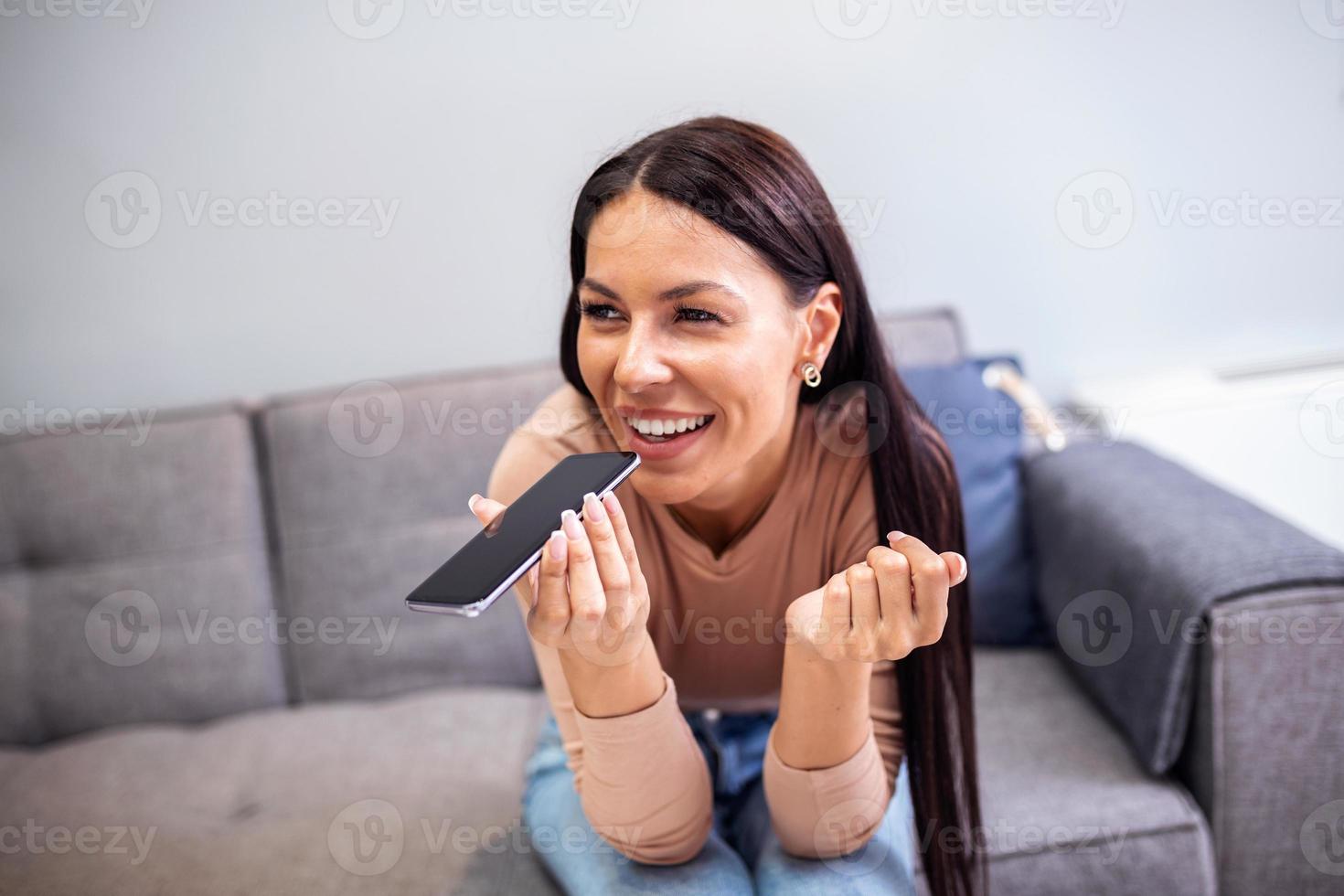 Woman sitting on couch holds phone talks on speakerphone with friend, makes voice recognition or request uses internet services through virtual assistant, record audio message, translator app concept photo