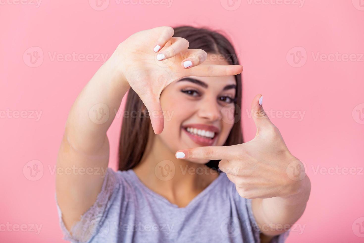 Happy young woman making frame gesture with fingers over pink background. Portrait of a happy smiling woman framing her face with her hands isolated photo