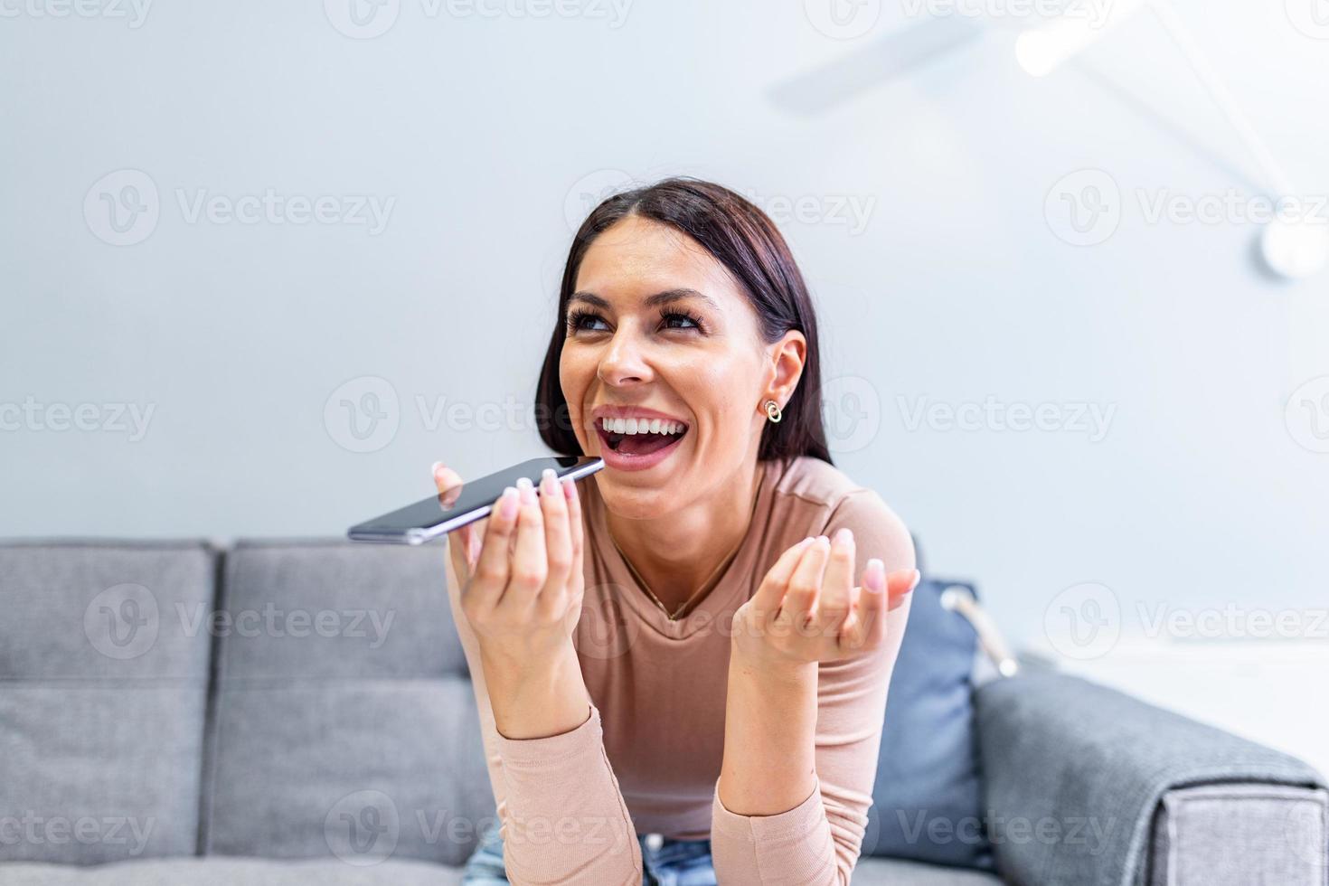 Woman sitting on couch holds phone talks on speakerphone with friend, makes voice recognition or request uses internet services through virtual assistant, record audio message, translator app concept photo