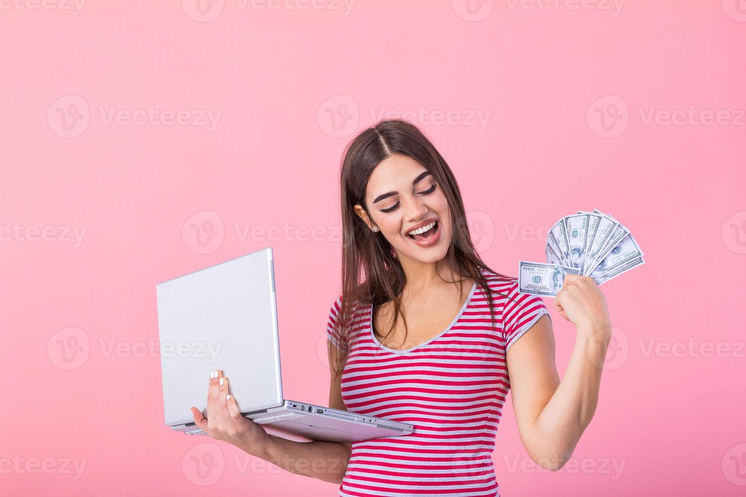 Image of cheerful young woman standing isolated over pink background using laptop computer and holding money banknotes . Portrait of a smiling girl holding laptop computer photo