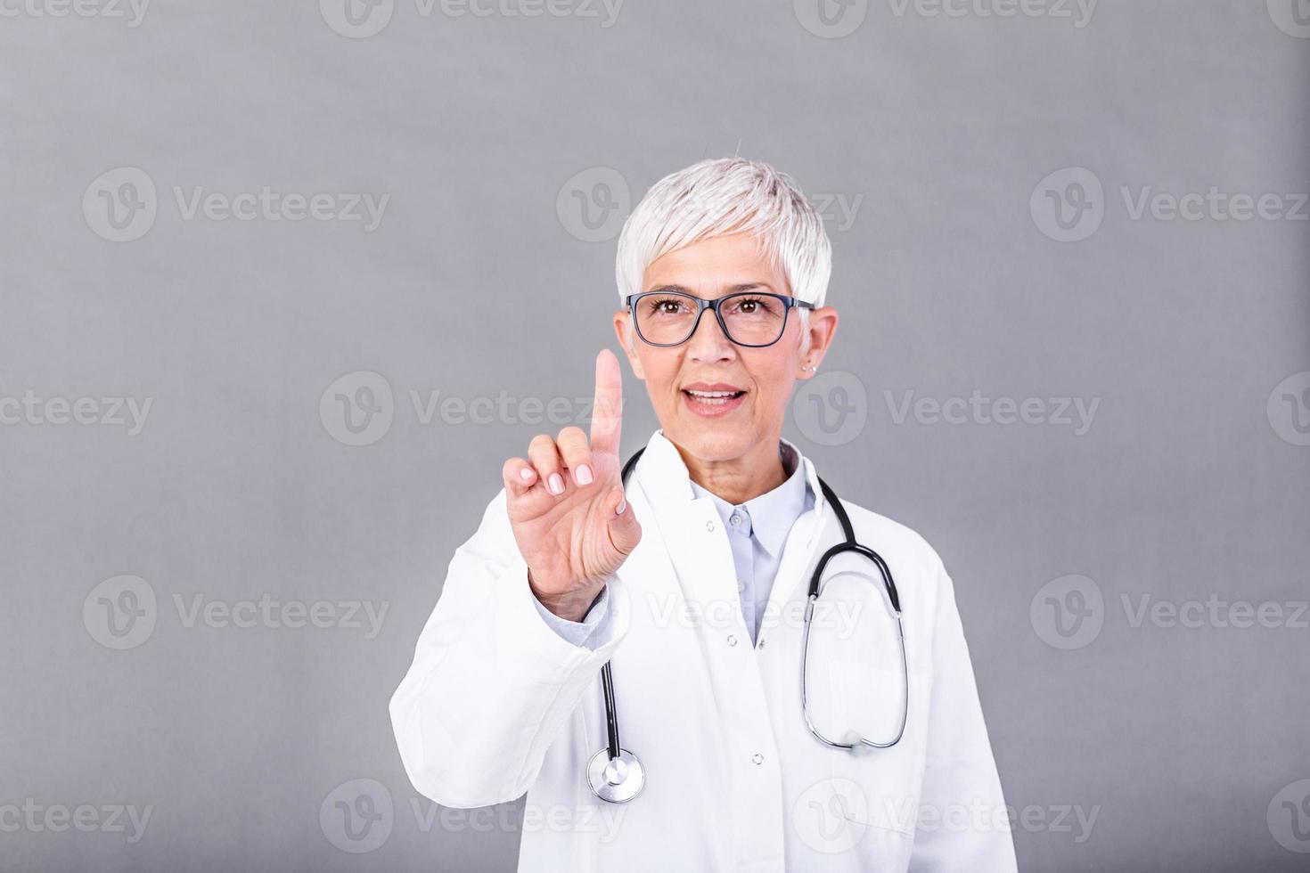 Mature woman doctorc is working with touch screen. Beautiful senior doctor is in a white uniform, stethoscope, on background isolated photo