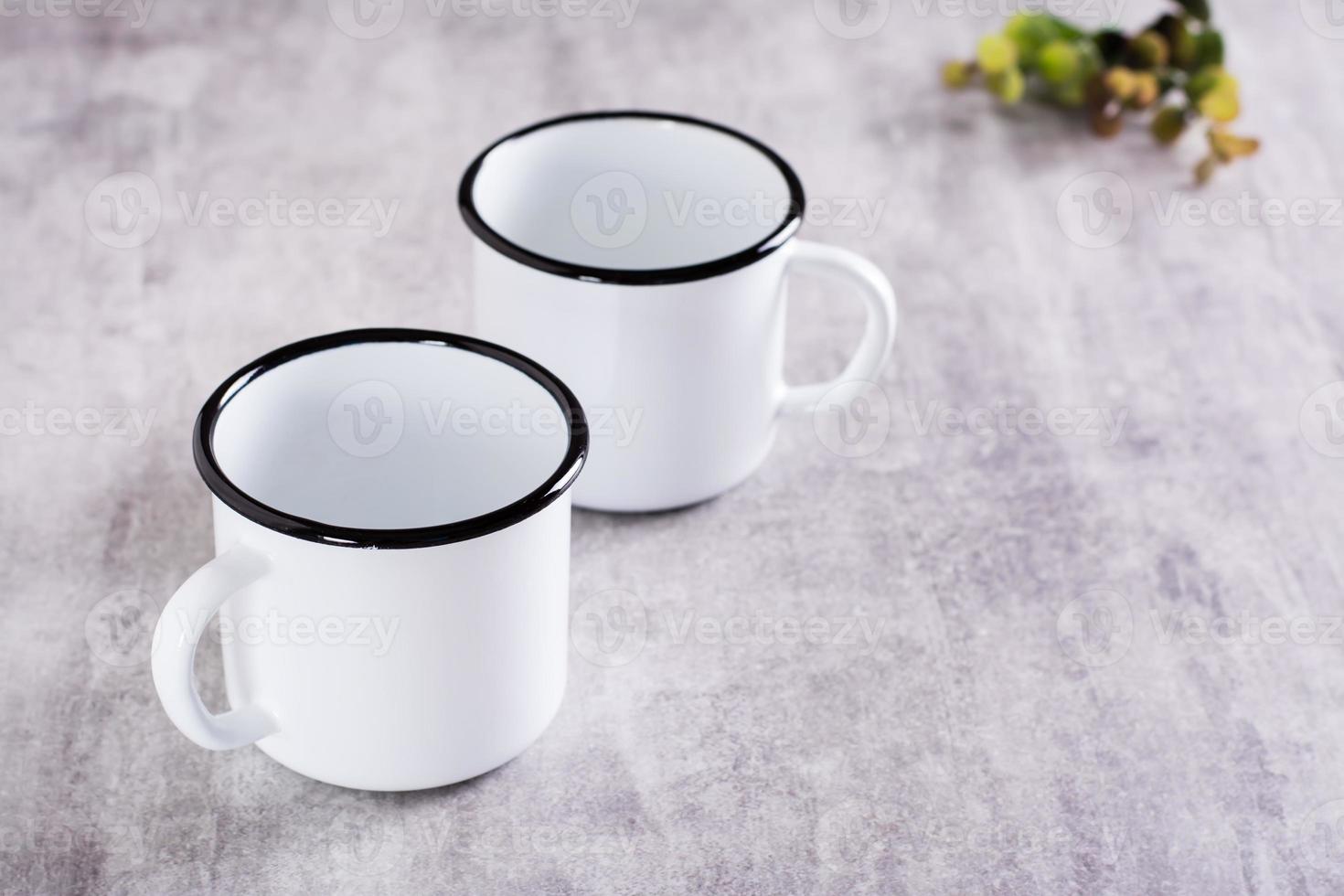 Two white empty metal mugs on a gray background with a place for an inscription photo