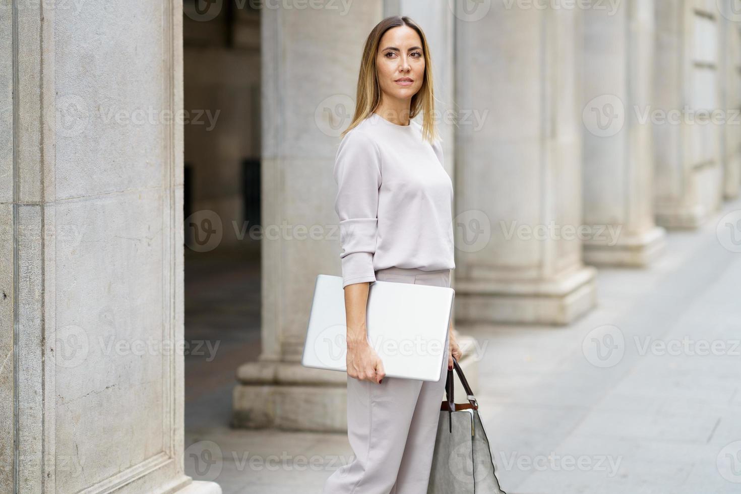Confident businesswoman with laptop on street photo