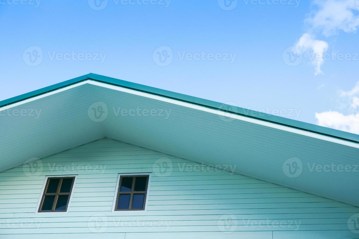 Symmetric detail shot of green roof gable showing ventilation panel with blue sky photo