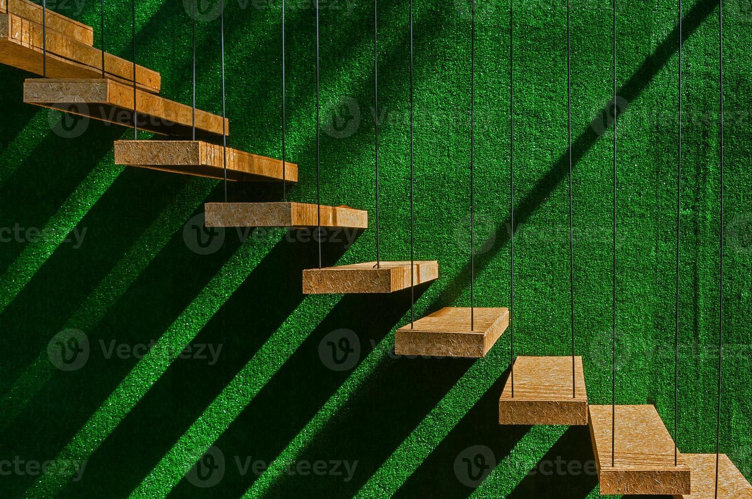 Hanging wooden stairs on artificial grass wall background Apartment staircase made of cables and wood apparently floating. photo