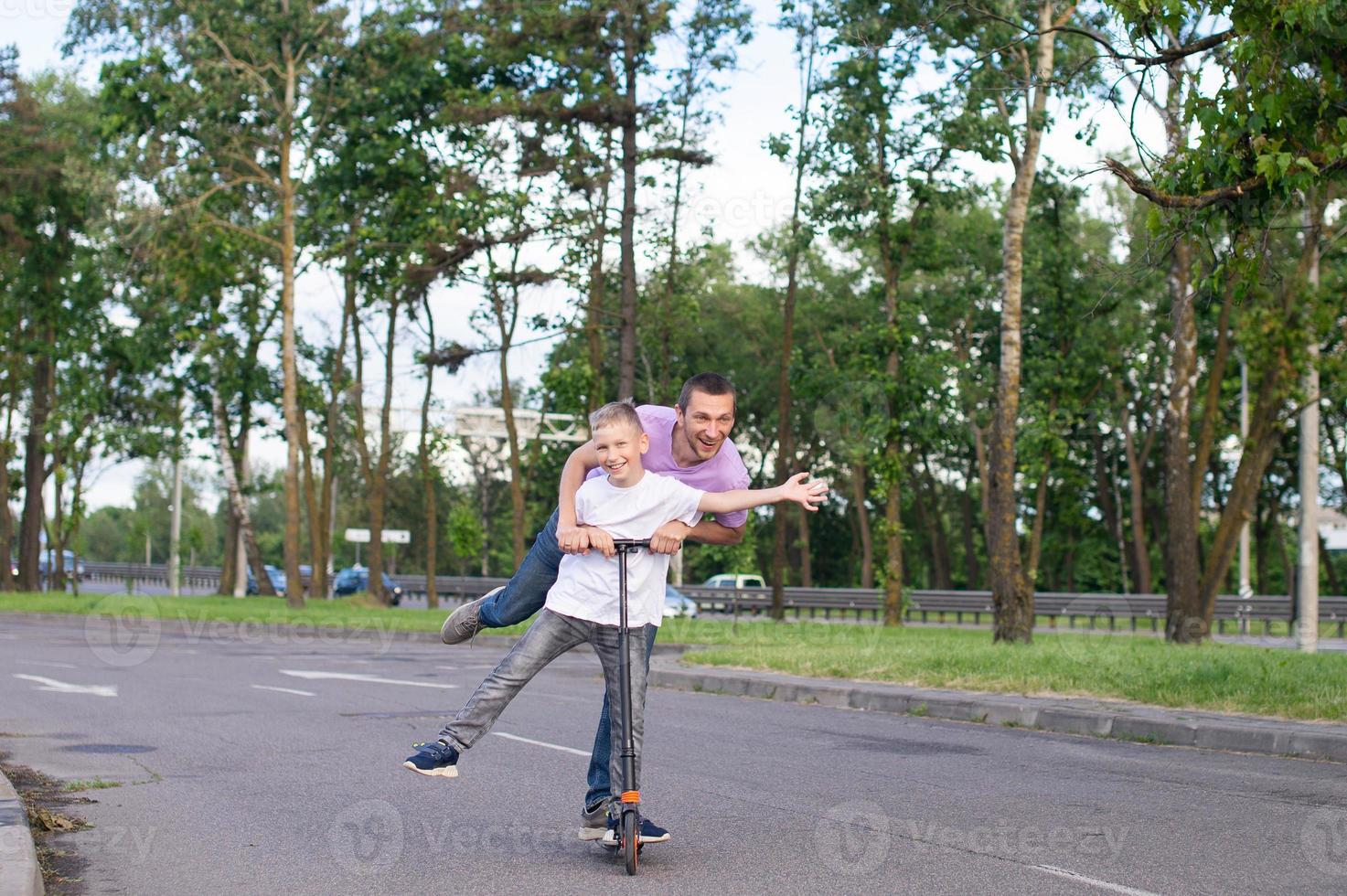 A father rides his son in a white T-shirt on a scooter, the happy child spread his hands photo