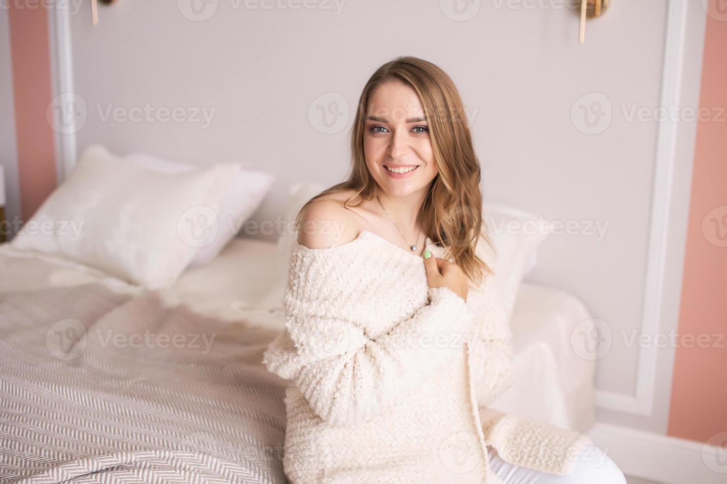 A cute girl in home clothes with an open shoulder is sitting on the bed photo