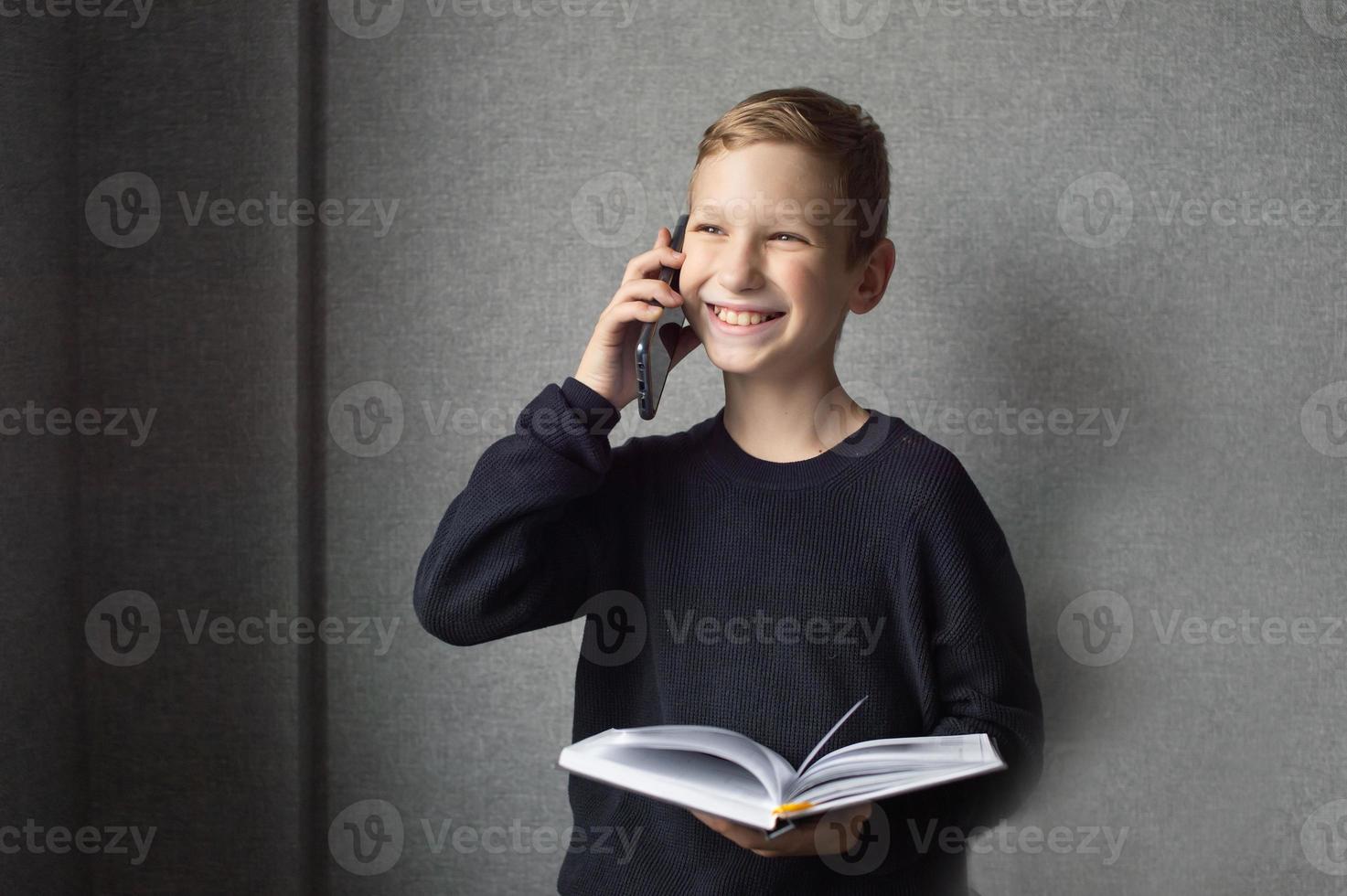 A happy boy is holding a book in his hands and talking on the phone photo