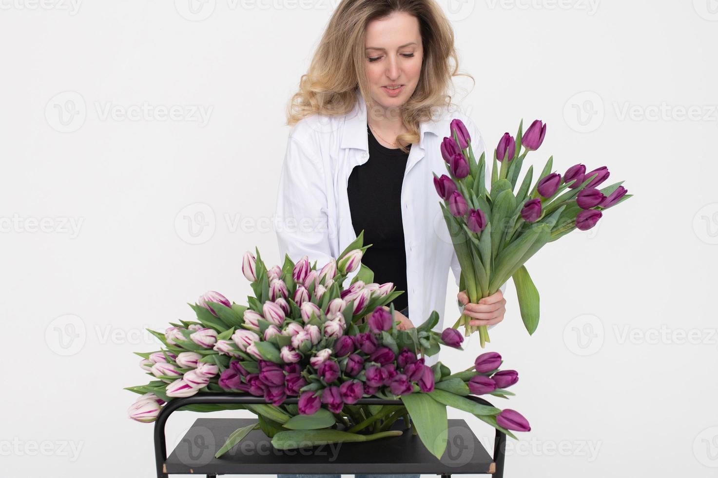 un linda niña elige un púrpura tulipán para un ramo de flores en el mesa. soportes en un blanco antecedentes foto