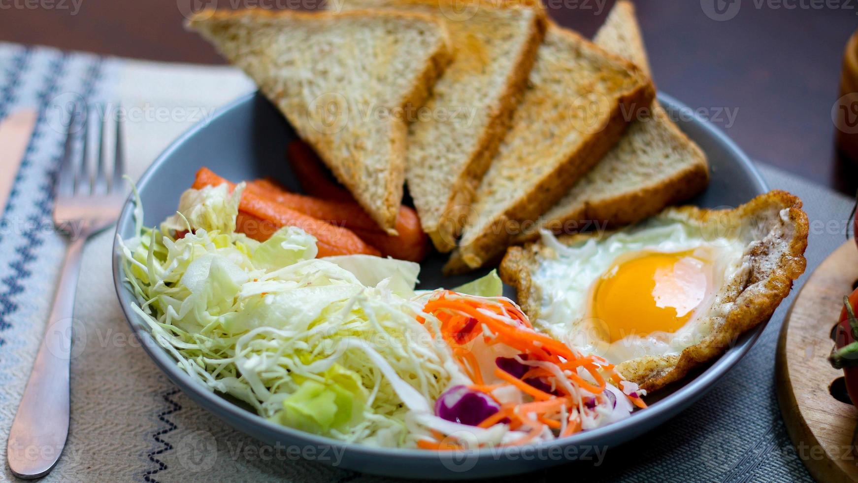 Breakfast, fried eggs, fried sausage, vegetable salad and toast on a brown wooden table with coffee. photo