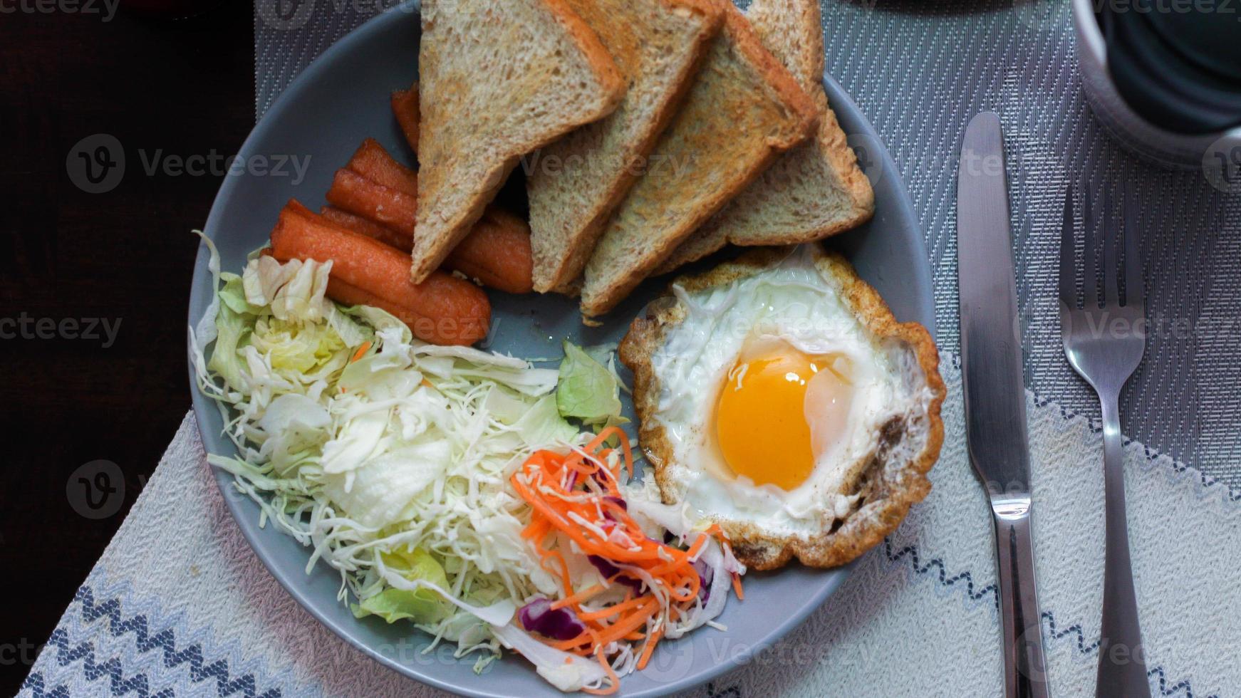 Breakfast, fried eggs, fried sausage, vegetable salad and toast on a brown wooden table with coffee. photo