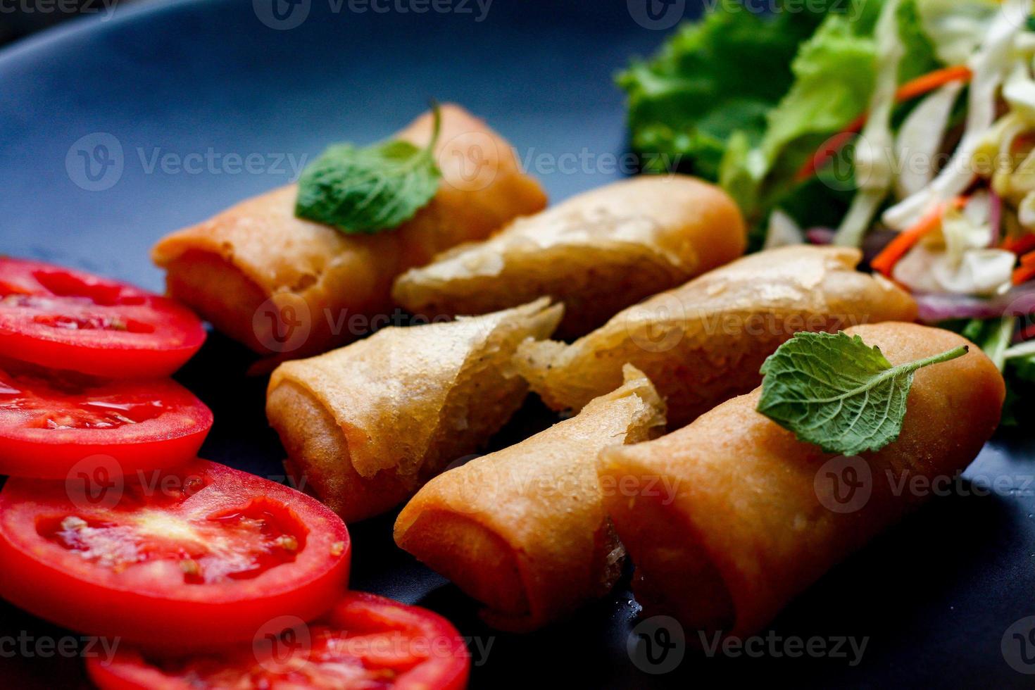 frito primavera rollos con vegetales y Tomates metido en un negro plato en un negro de madera mesa y inmersión salsa. foto