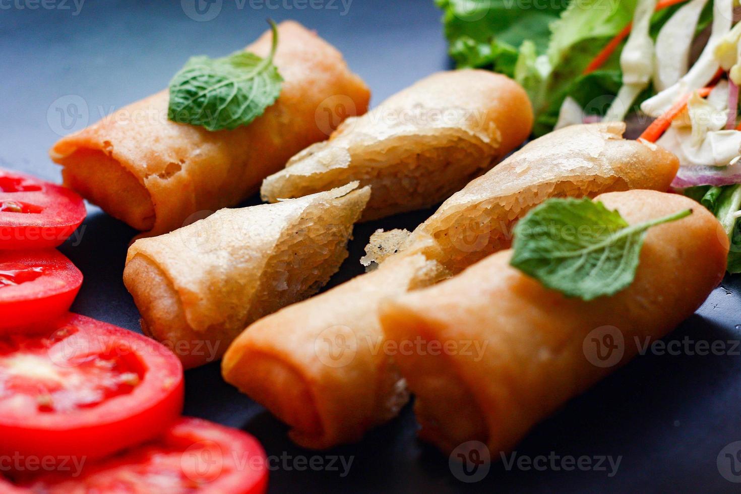 Fried spring rolls with vegetables and tomatoes placed in a black plate on a black wooden table and dipping sauce. photo