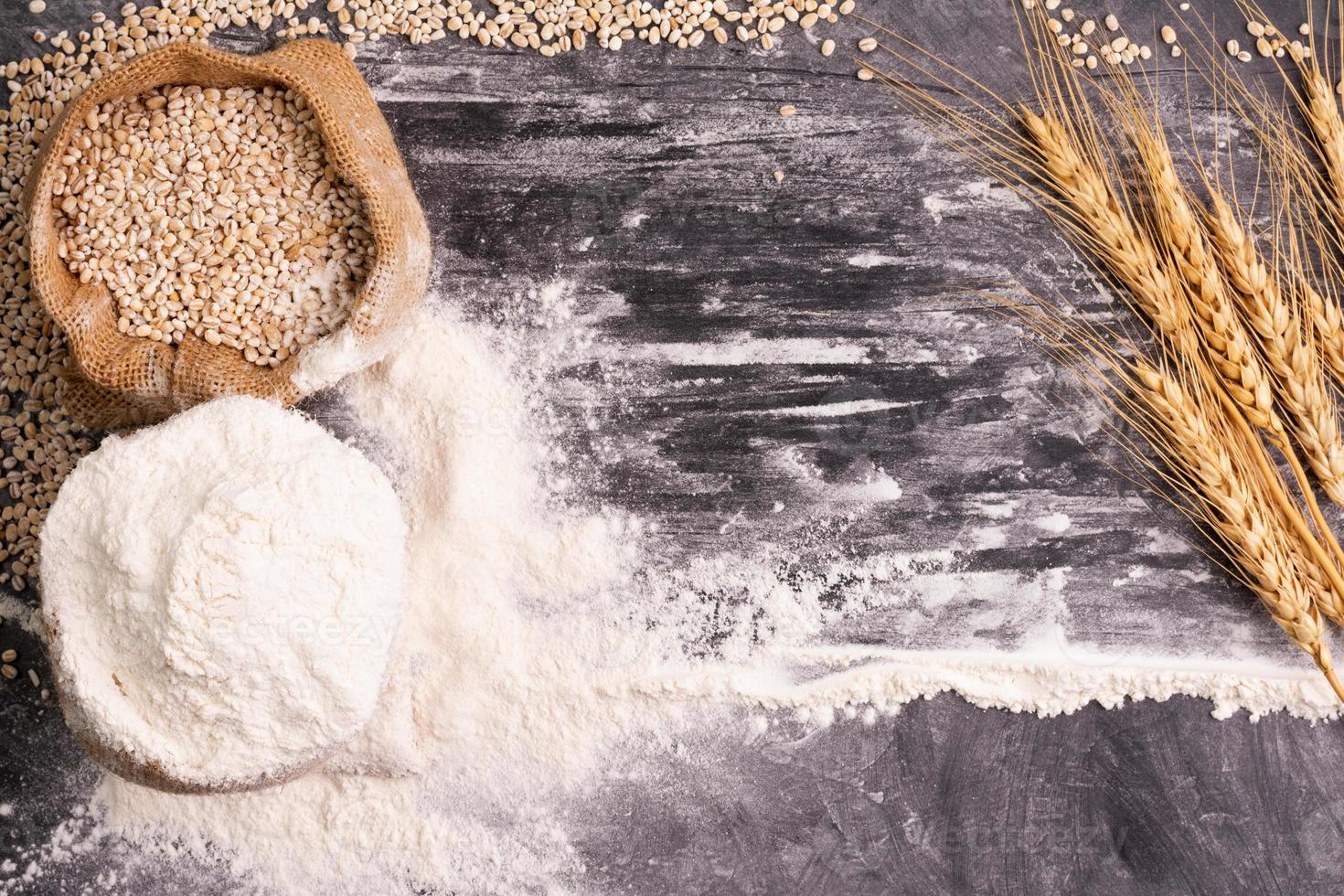 harina y trigo granos en sacos con trigo orejas en un negro antecedentes mesa. en un rústico cocina. parte superior vista. foto