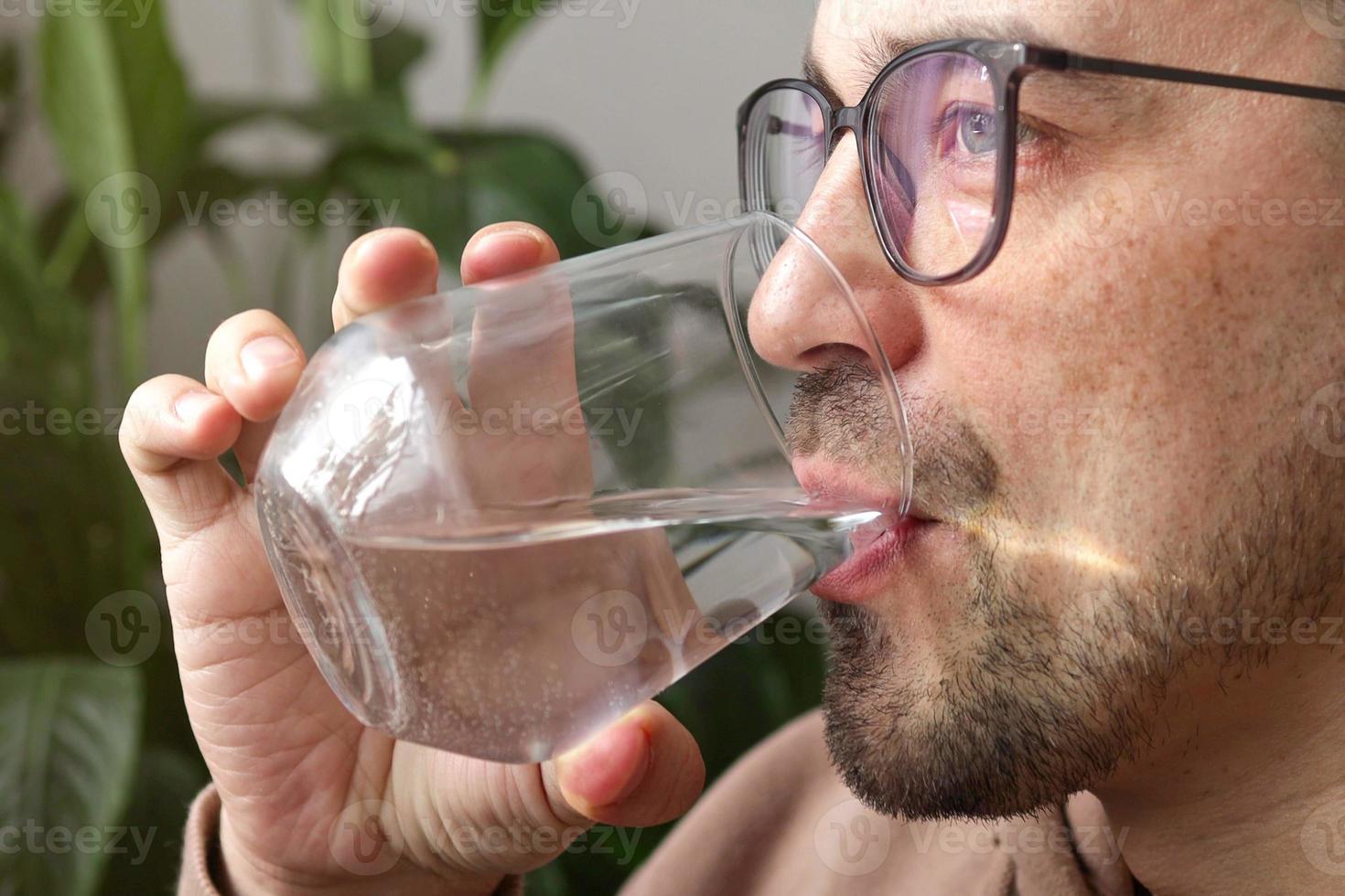 Handsome man in glasses drinking fresh glass of water at home. photo