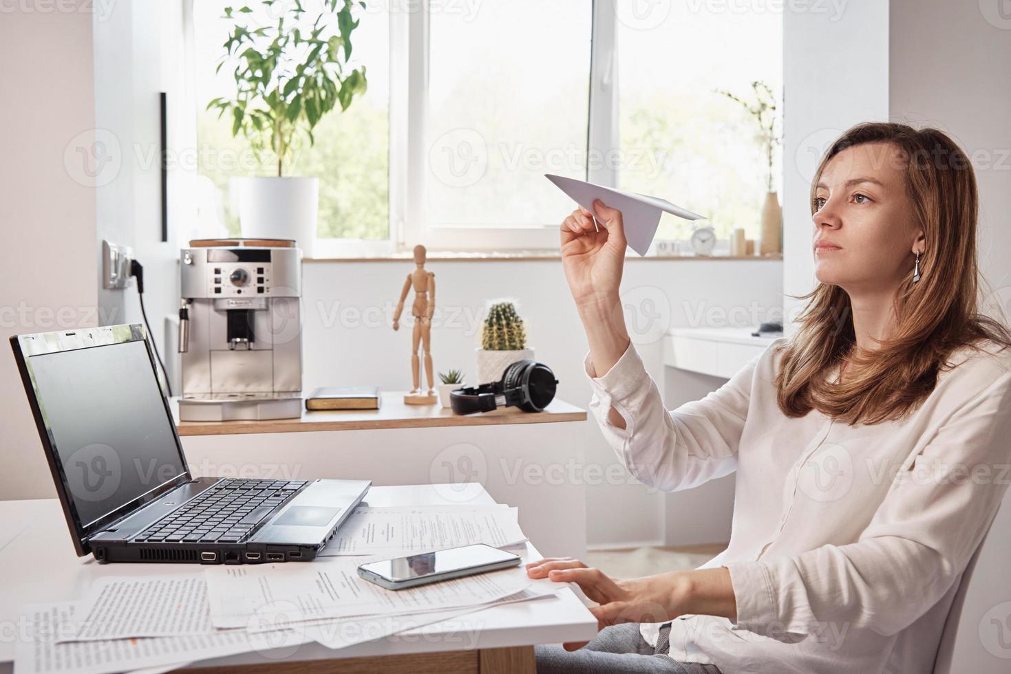 Woman plays with paper plain at home office. Procrastinate at remote work photo