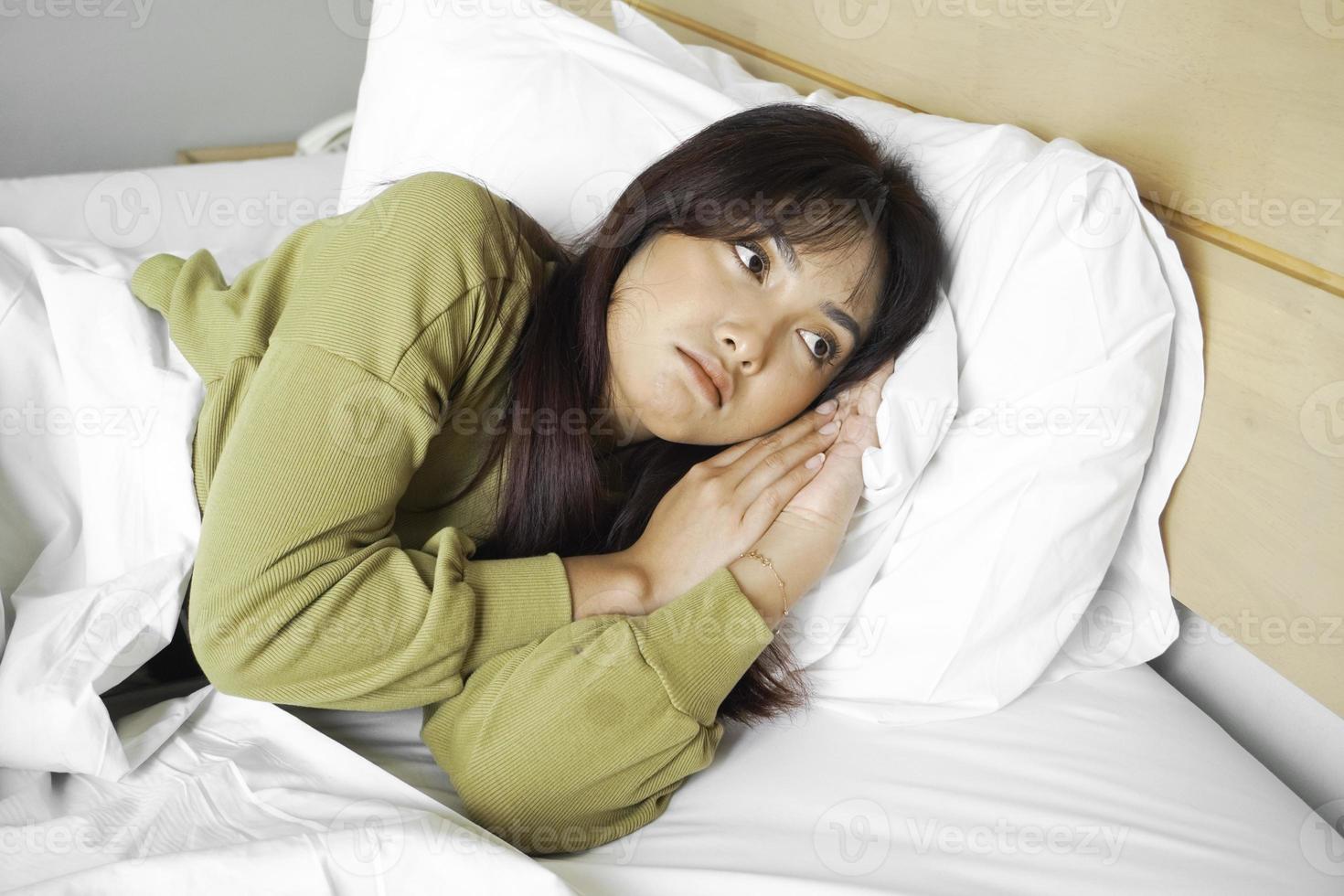 Thoughtful Asian woman looks pensively above dressed in sweatshirt poses thinks about future while lying on the bed photo