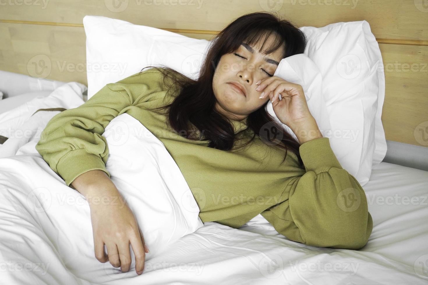 A sad young Asian woman is crying while lying on the bed photo