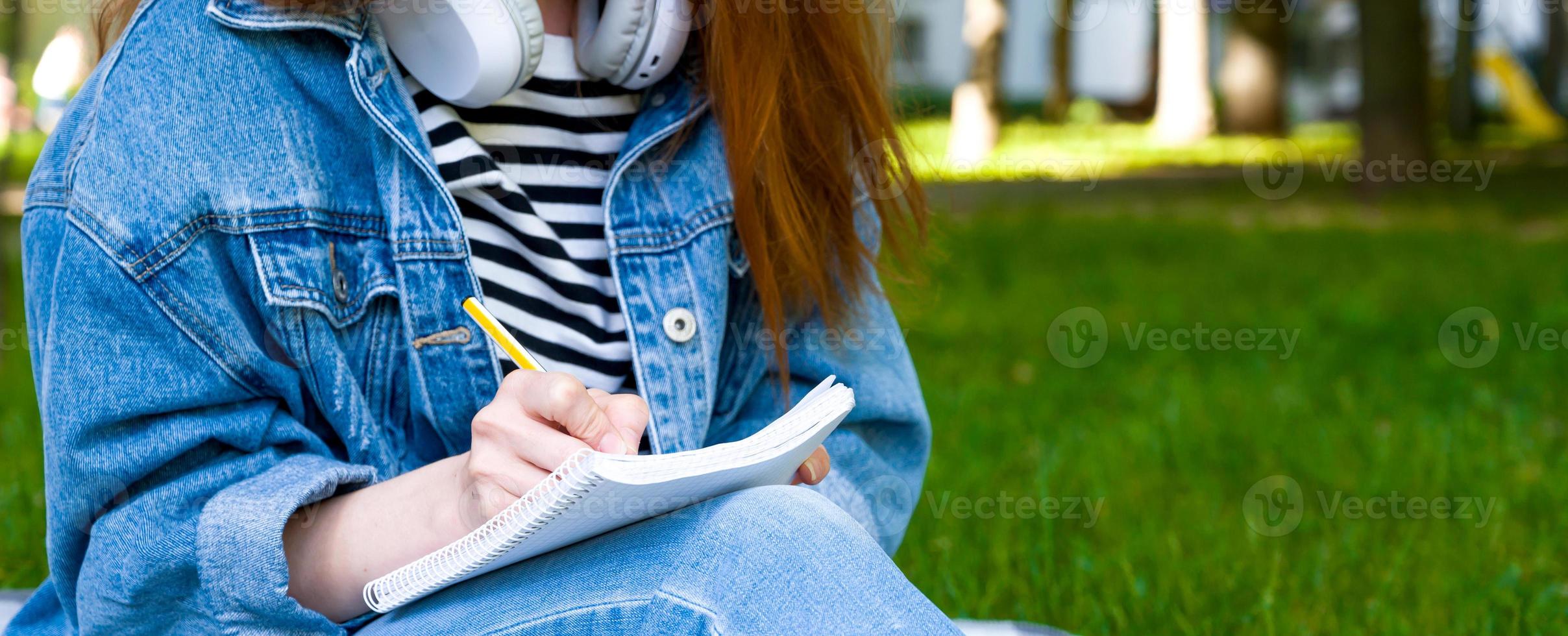 Unrecognizable girl takes down notes in notebook in the park.Distant learning. University,college,school education photo