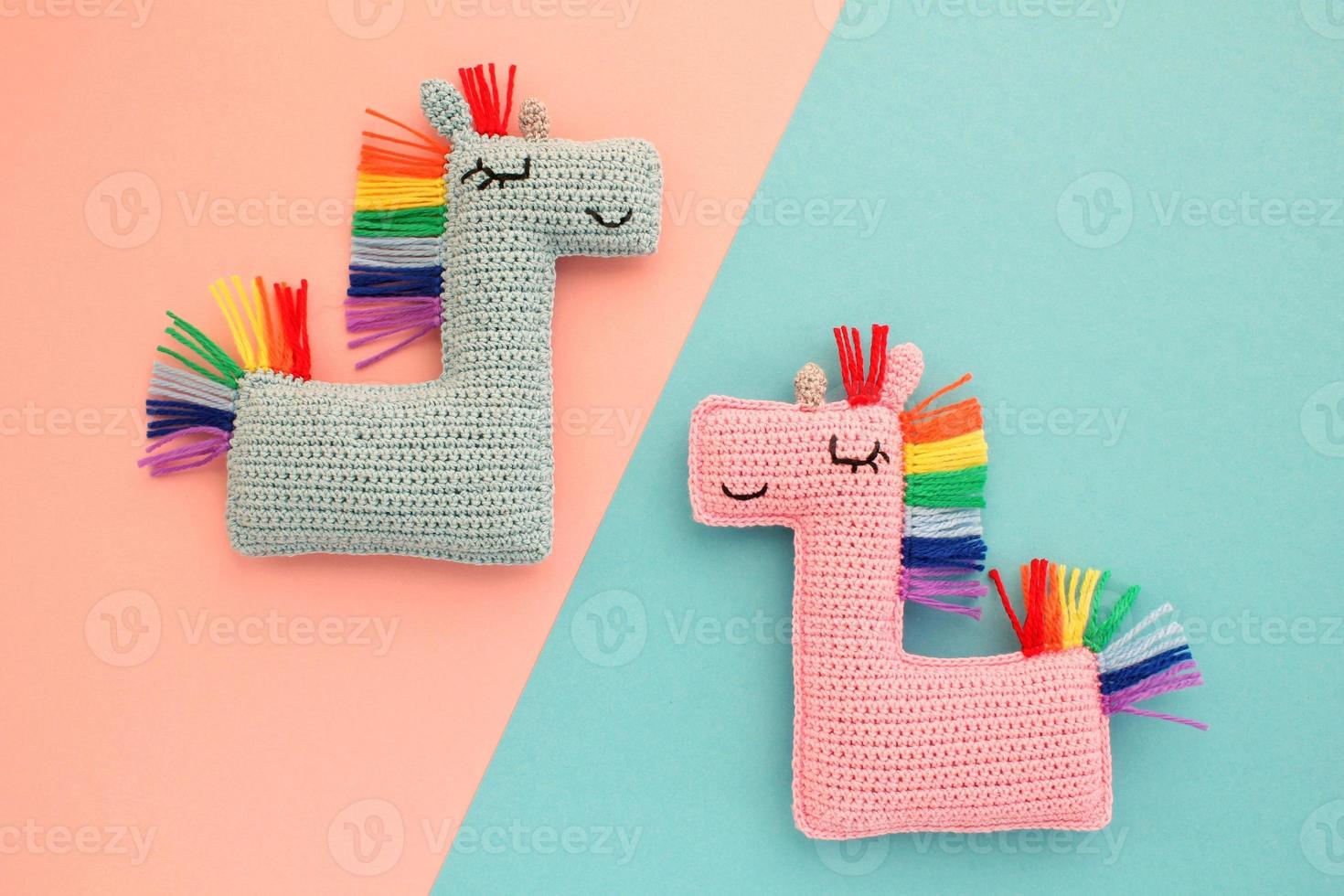 Crochet amigurumi handmade stuffed soft colored unicorn toys with rainbow mane on pink and blue background. Handwork, hobby. Craft diy newborn pregnancy concept. Knitted doll for little baby. Close-up photo