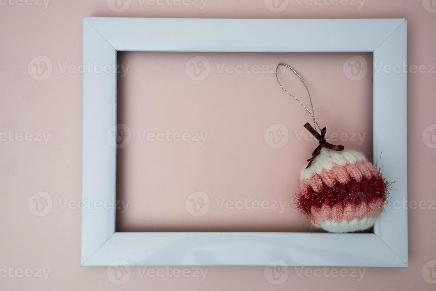 knitted, soft, handmade colored Christmas ball and an empty photo frame on a light peach background