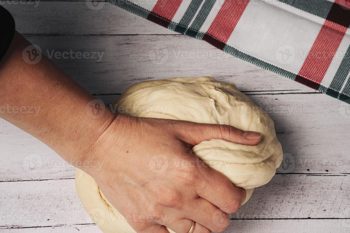 The chef's hands prepare and knead fresh homemade pizza dough on the kitchen table photo