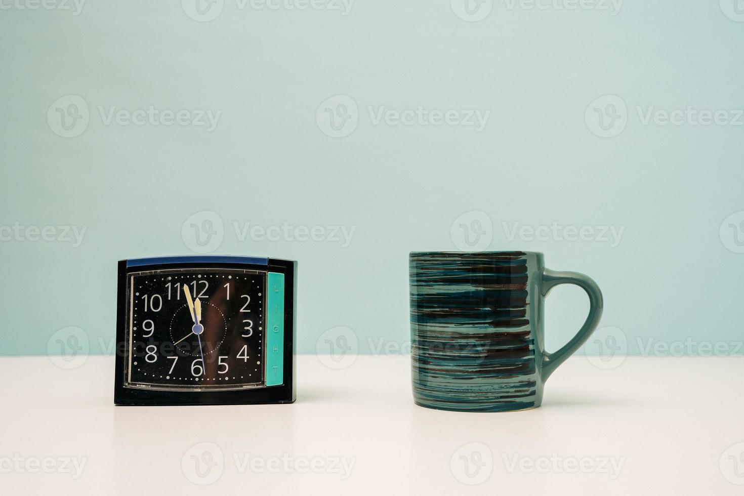 square modern alarm clock and mug on the table on a turquoise background photo