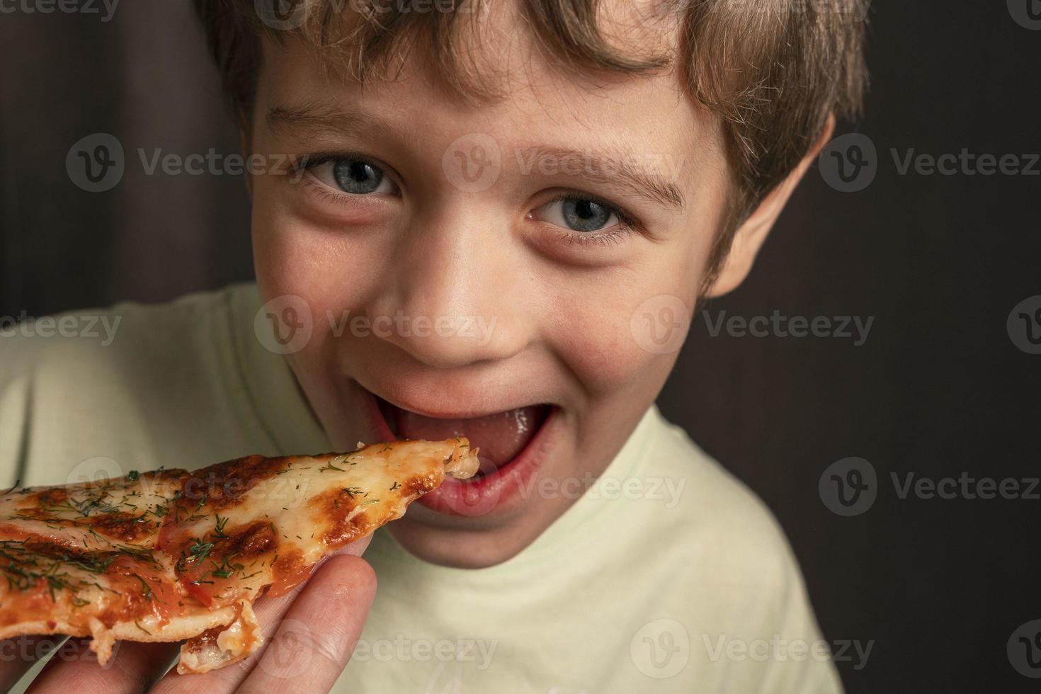 caucásico alegre chico come un pedazo de Pizza y mira a el cámara sonriente foto