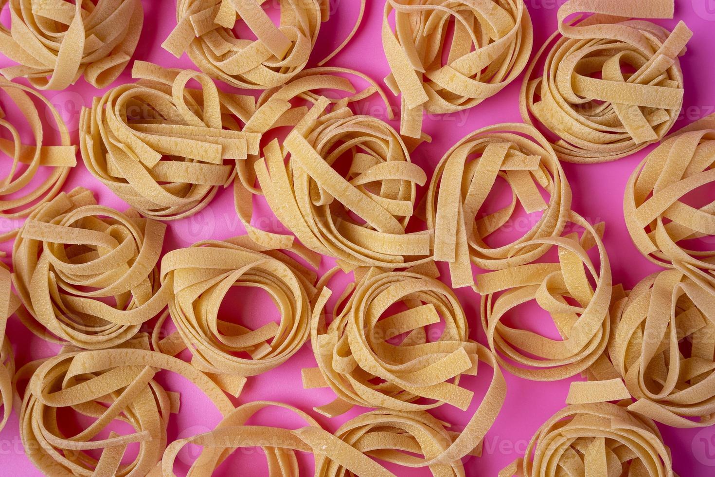 A pattern of Raw tagliatelle on a pink background, pasta nests, egg paste photo