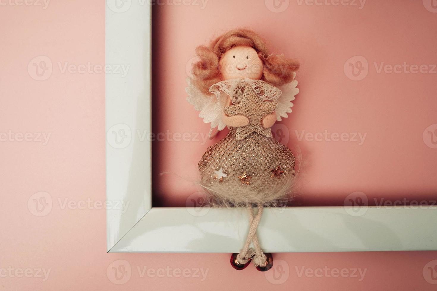 a figure of a funny angel sitting on the edge of an empty white photo frame