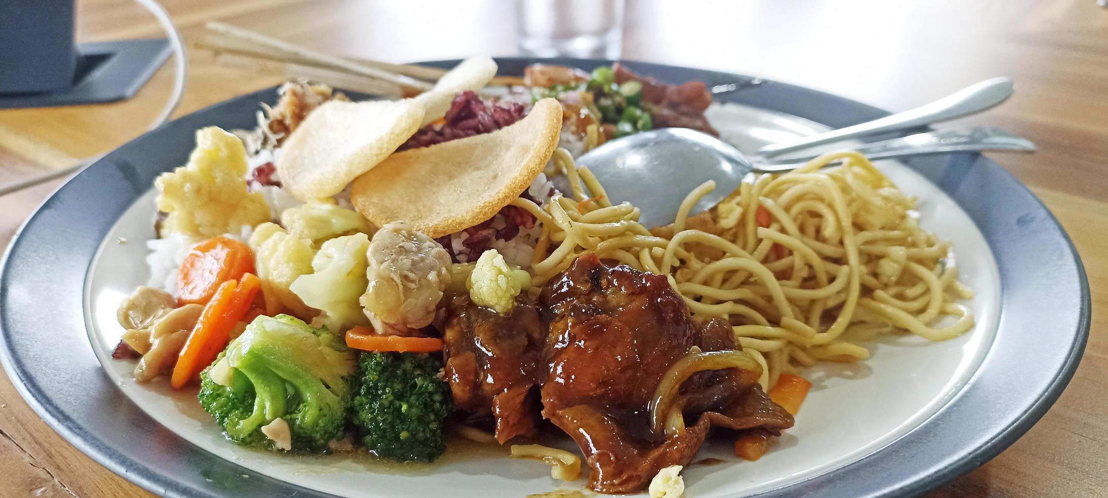 Rice dish with side dishes of chicken, cauliflower, broccoli, noodles and crackers in one plate photo