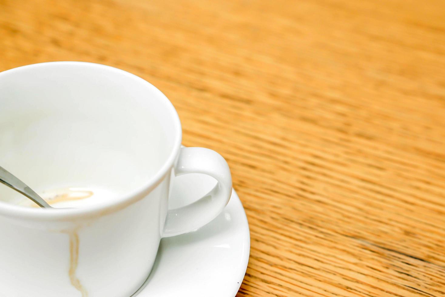 Coffee stain in white cup and coffee spoon with saucer on wooden table. photo