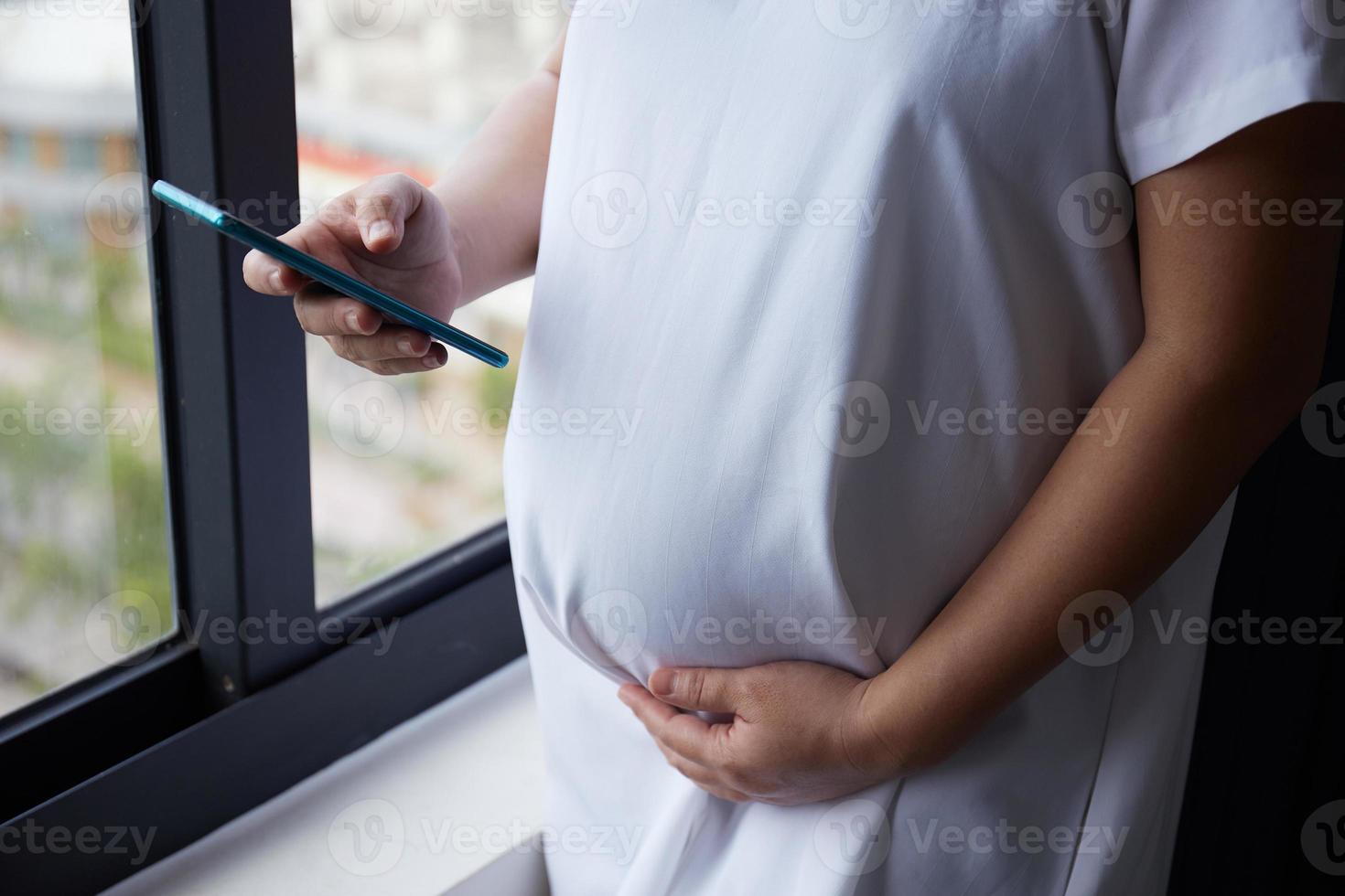 Young Asian Pregnant woman using smart phone for checking news while standing near the window photo