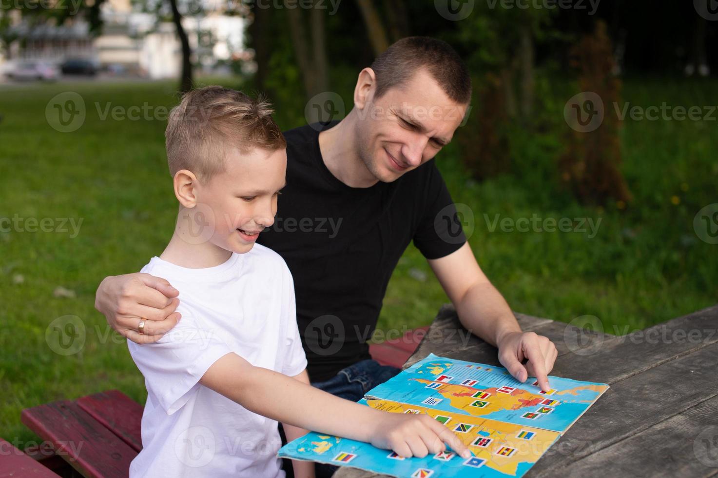 Cute boy in a white T-shirt shows a map of the world to Dad photo