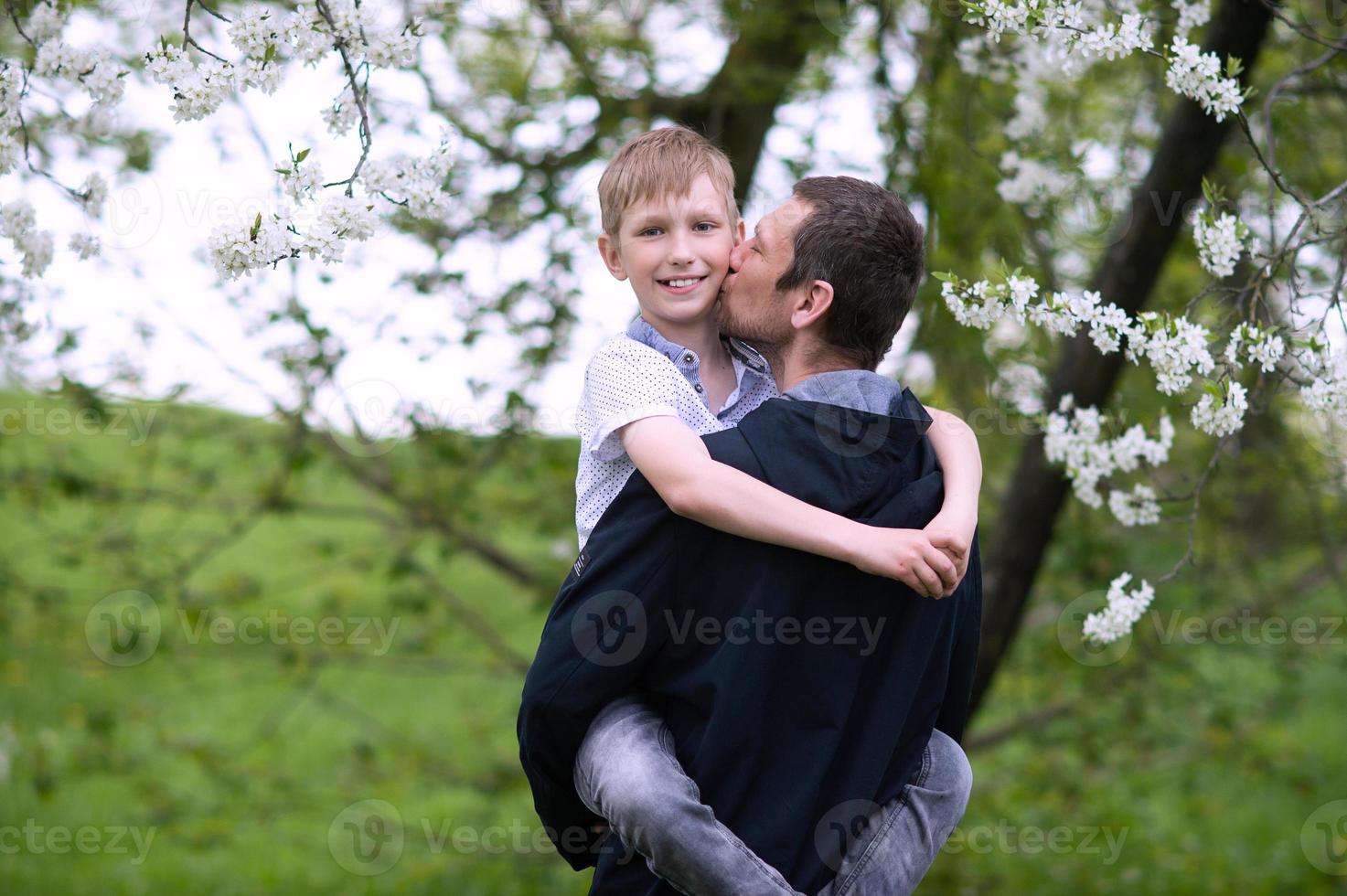 The boy in dad's arms looks into the camera and smiles, dad kisses his son photo