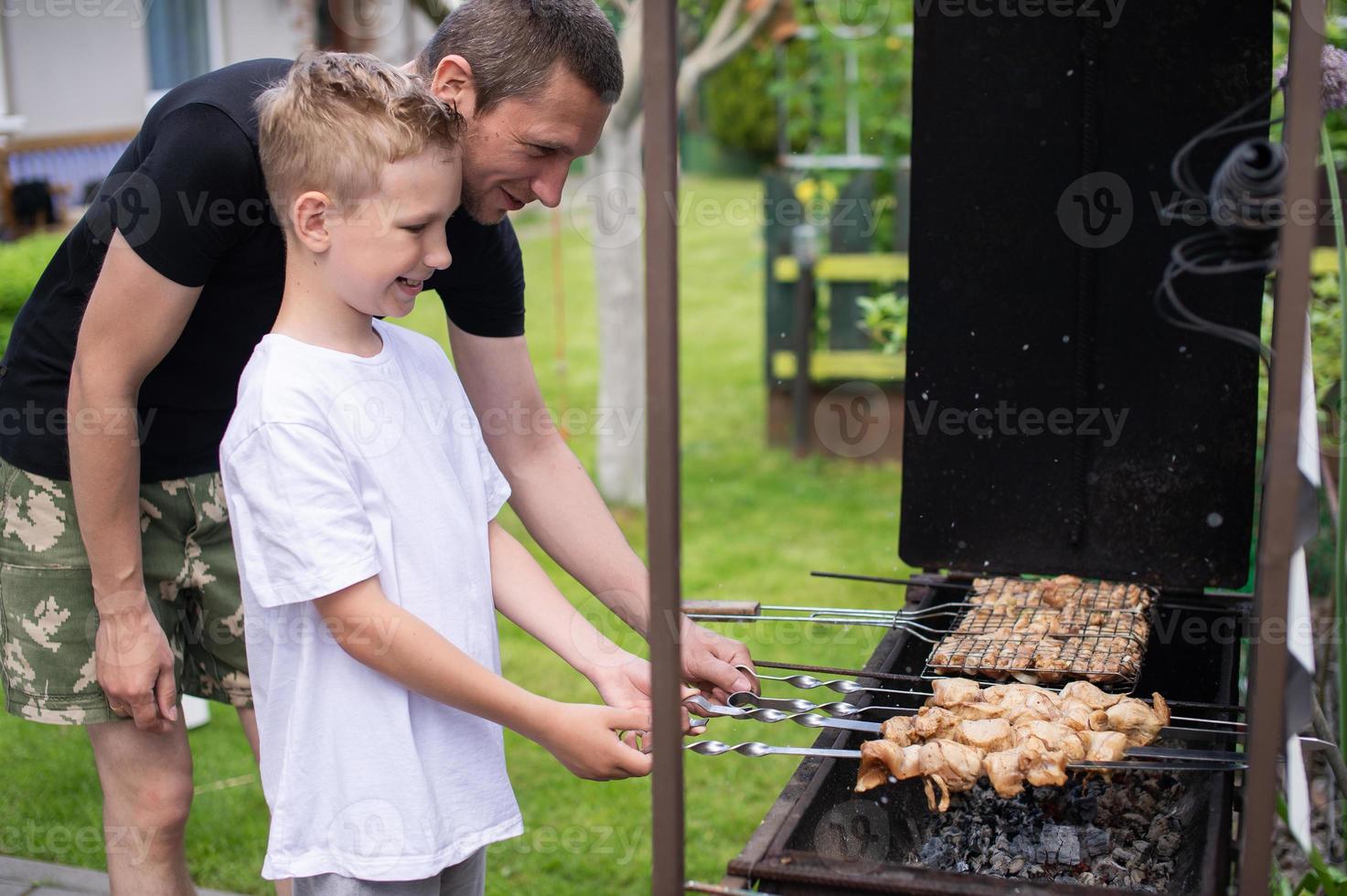 Cheerful dad and son roast meat on the grill photo