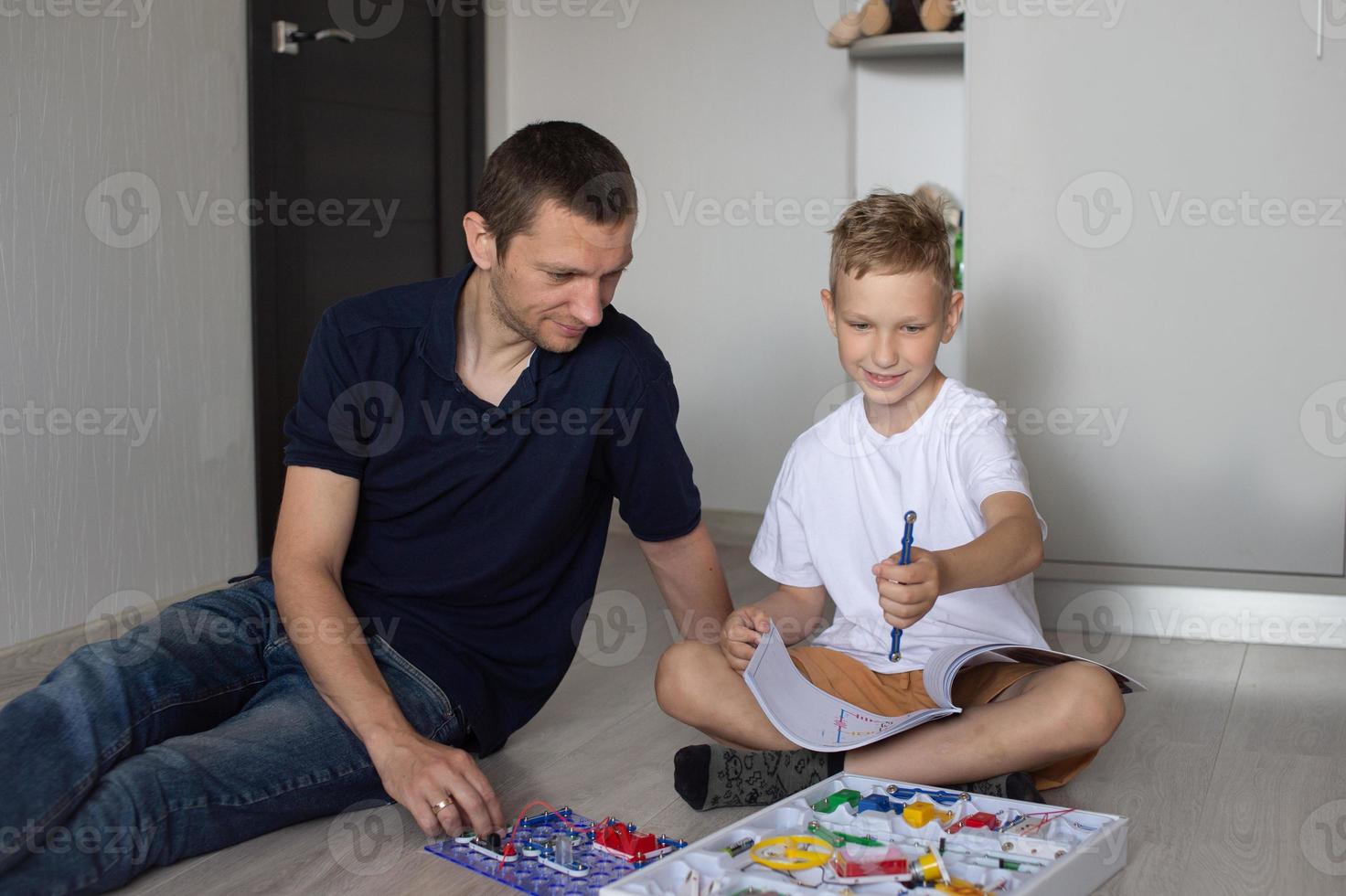 A cute boy in a white T-shirt collects an electrical designer with his dad in the room photo