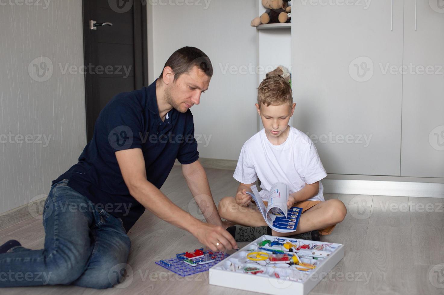 A cute boy in a white T-shirt collects an electrical designer with his dad in the room photo