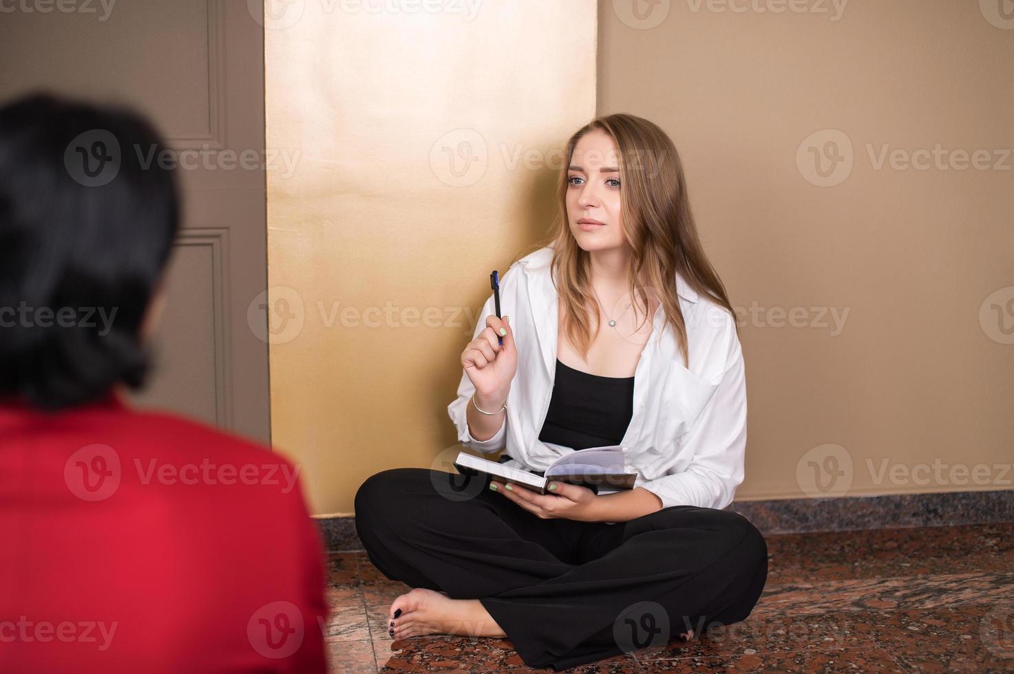 A cute girl is sitting on the floor with bare feet and holding a pen with a notebook in her hands photo