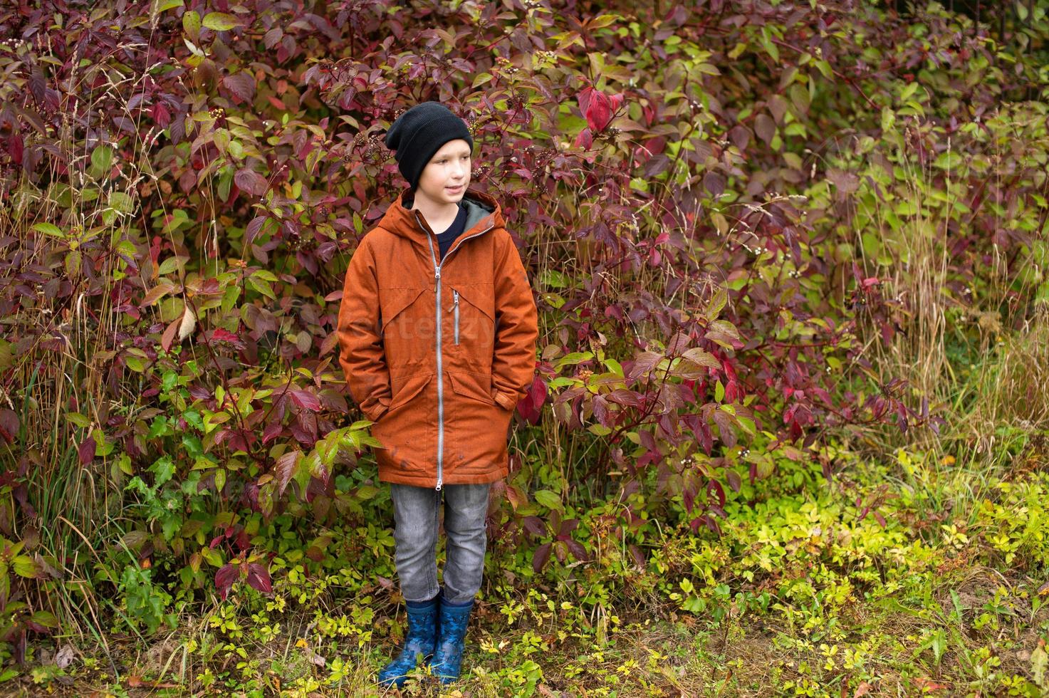 A cute boy in rubber boots stands in the autumn forest photo
