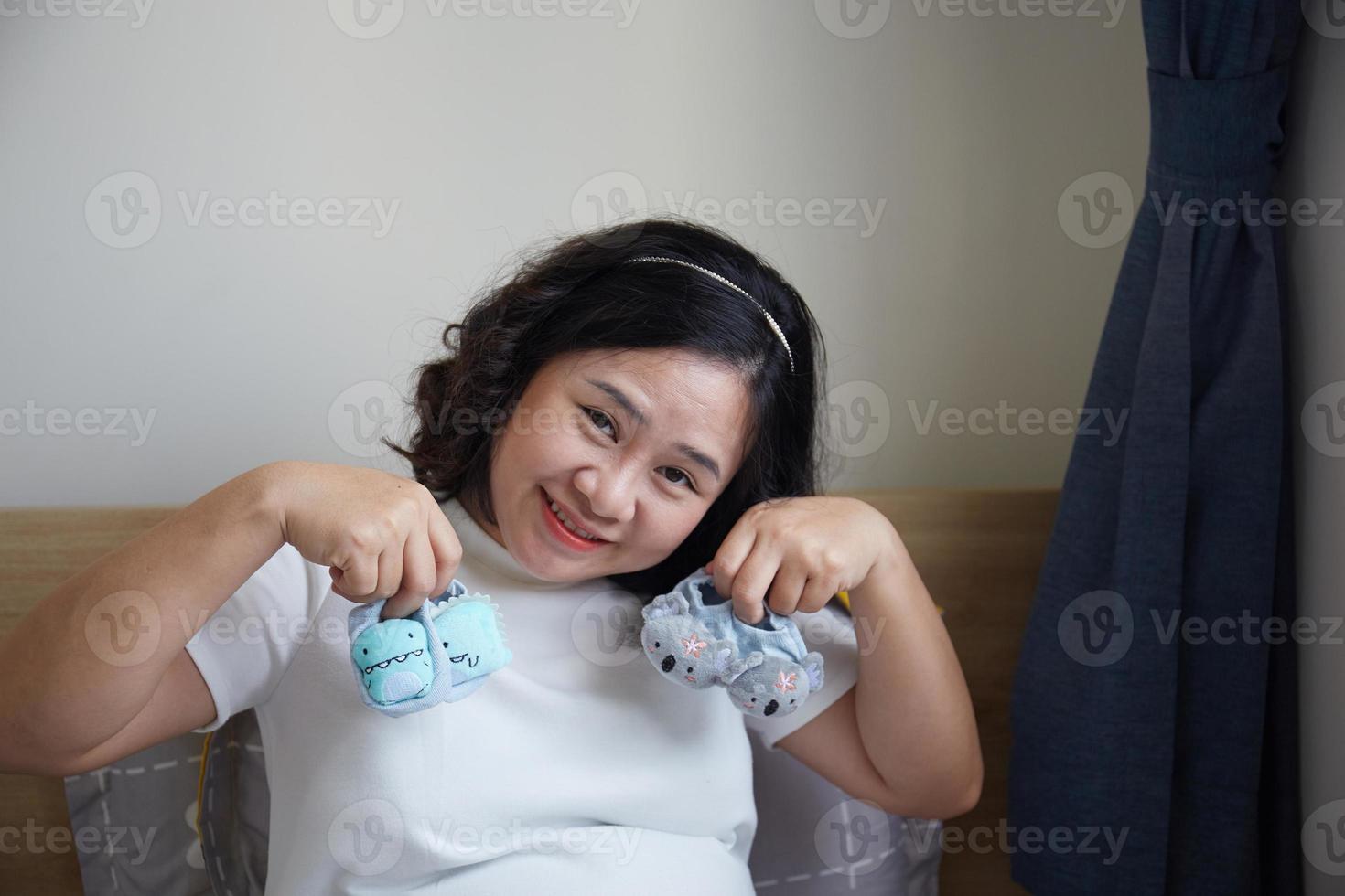 Young Happy Asian Pregnant holding small shoes for the unborn baby in her hand and look into the camera photo